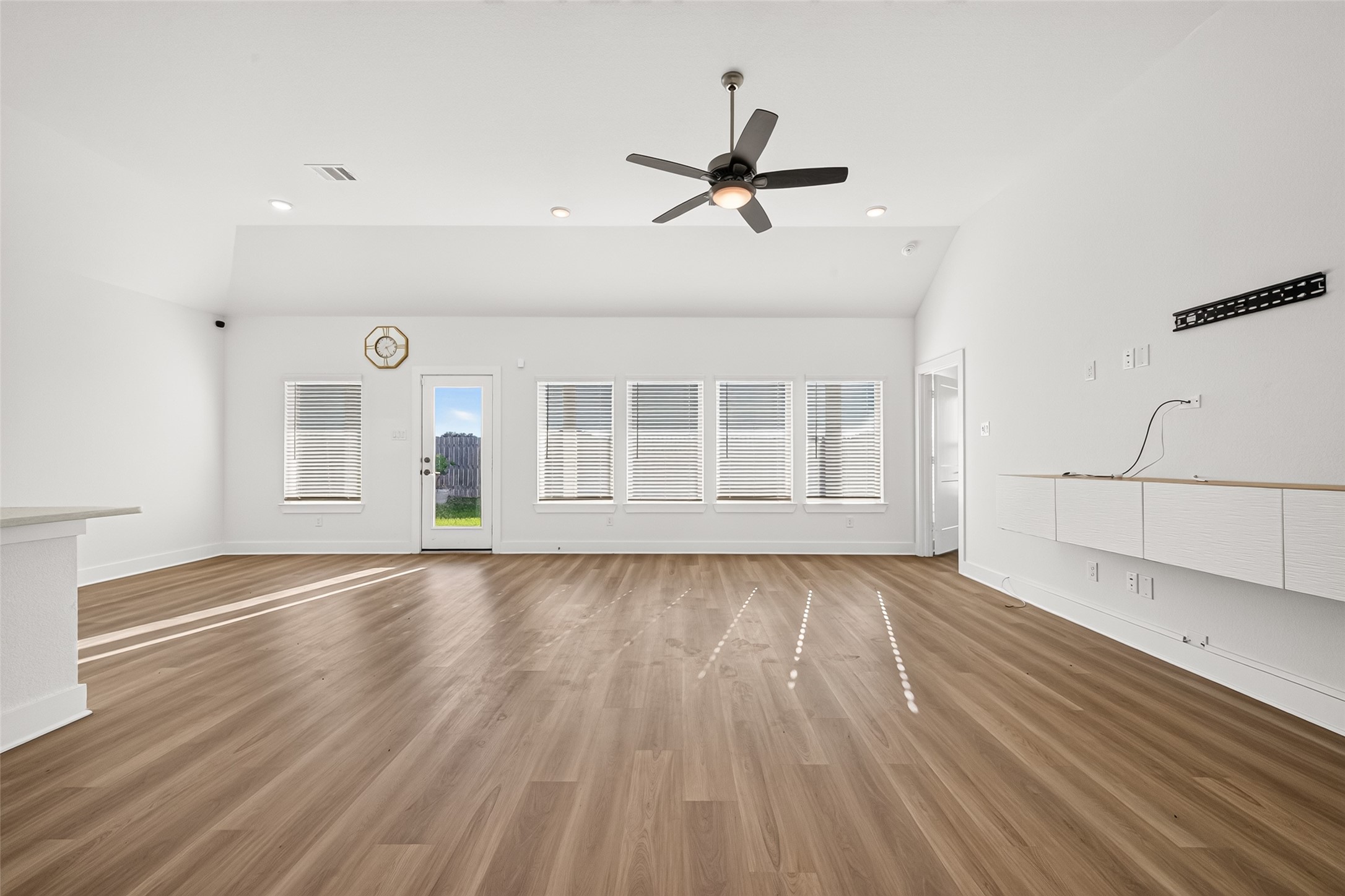 Living room with windows across the back wall, rear door to the yard, ceiling fan, and recessed lighting. Living room with windows across the back wall, rear door to the yard, ceiling fan, and recessed lighting.