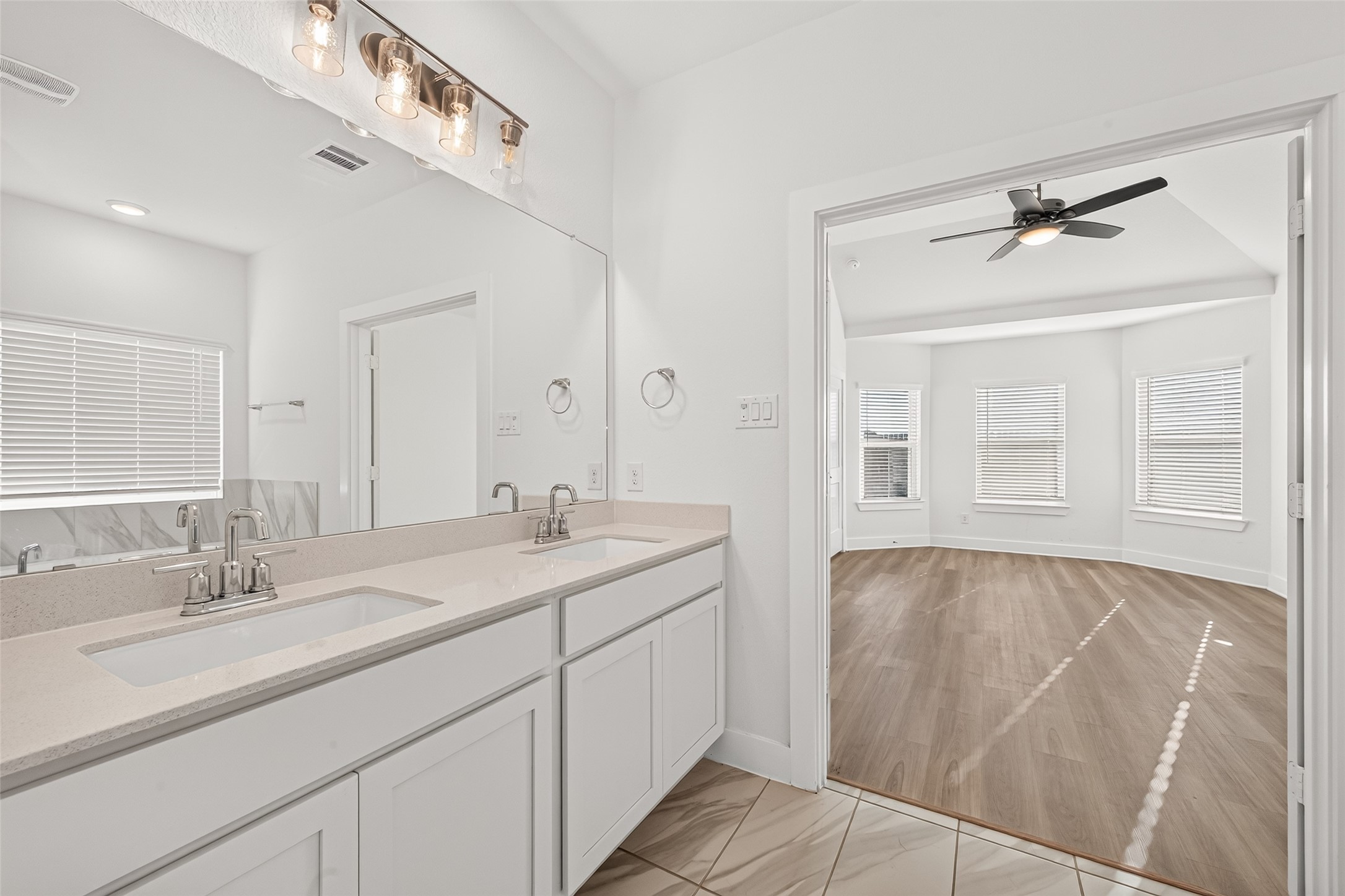 Primary bathroom double vanity with tile flooring and a view into the bedroom.