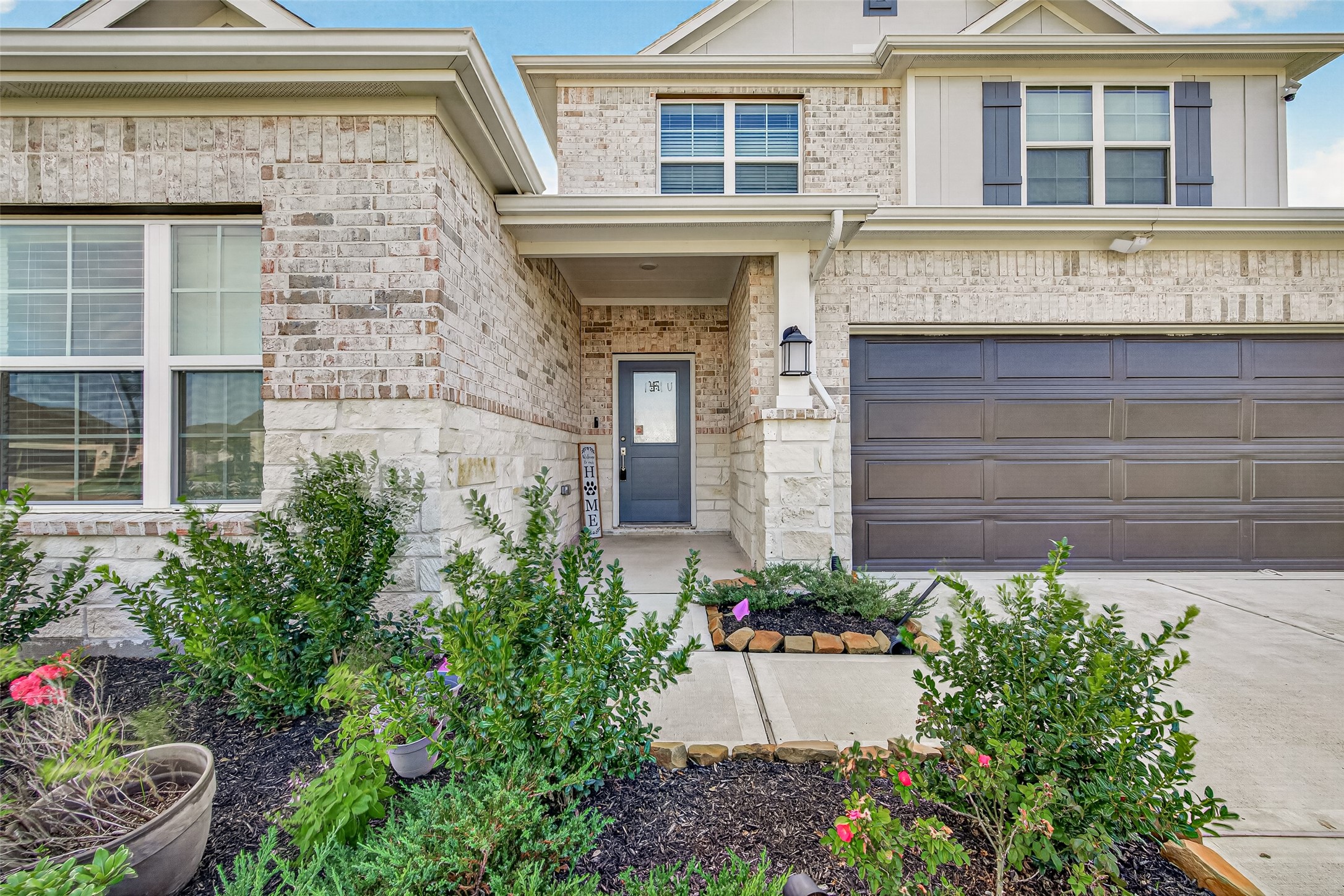 Front exterior with brick and stone facade, covered entry, two-car garage, and landscaped beds.