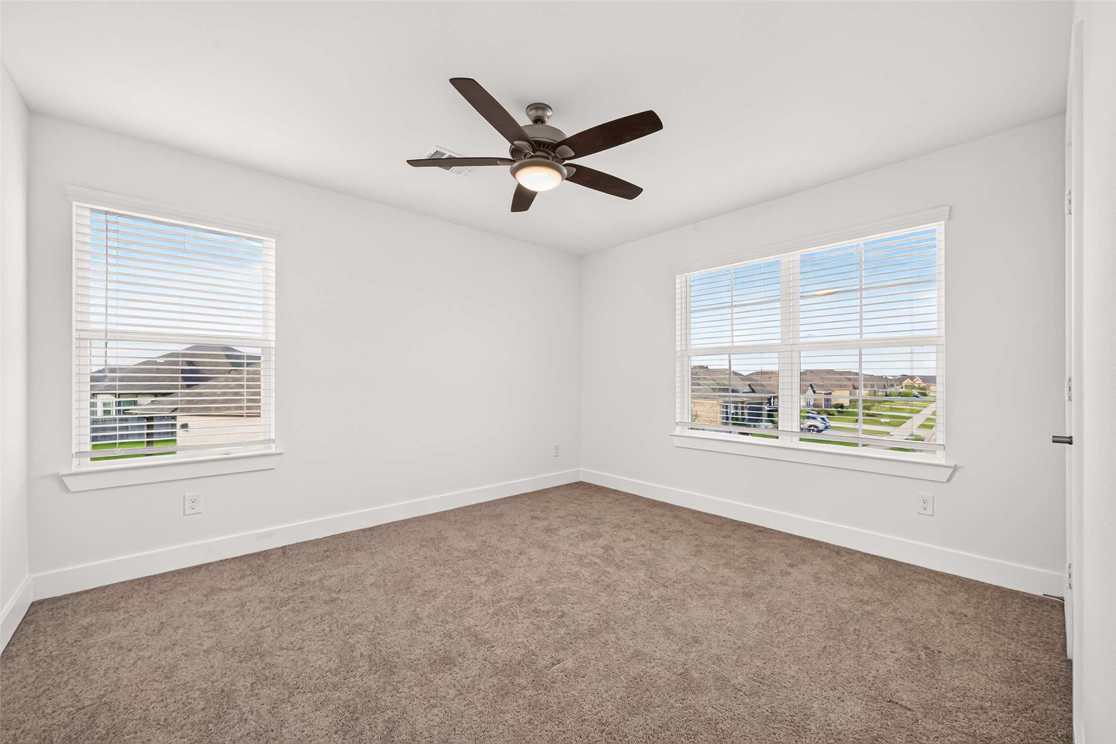 Upstairs bedroom with carpet, ceiling fan, and windows on two walls.