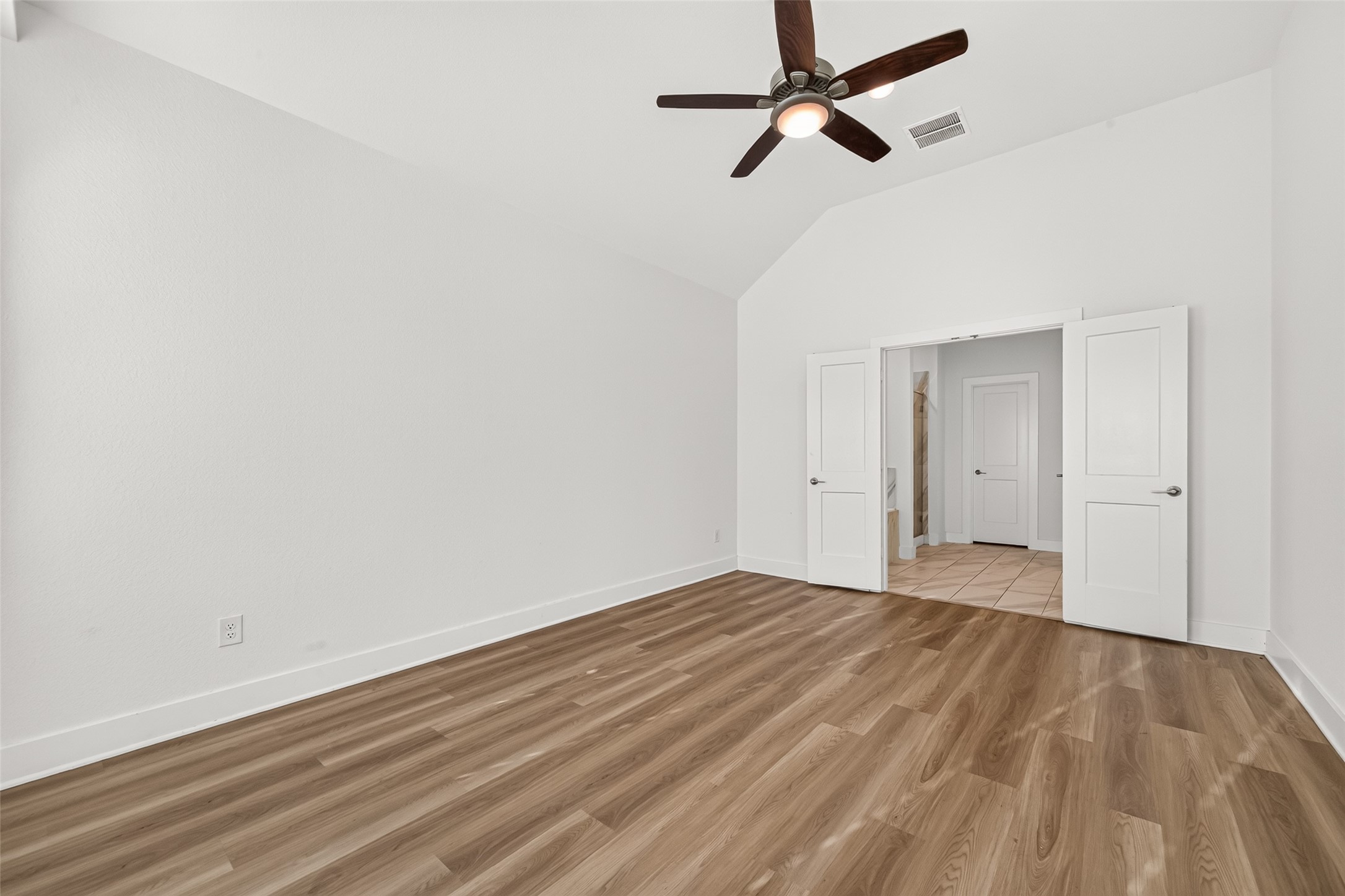Primary bedroom with vaulted ceiling and double doors to the hallway.