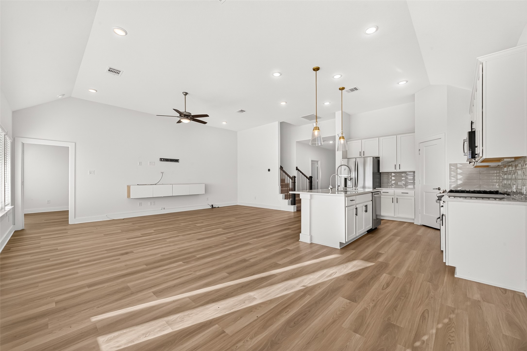 Wide view of the kitchen and living room showing the open layout, recessed lighting, and wood-look flooring.