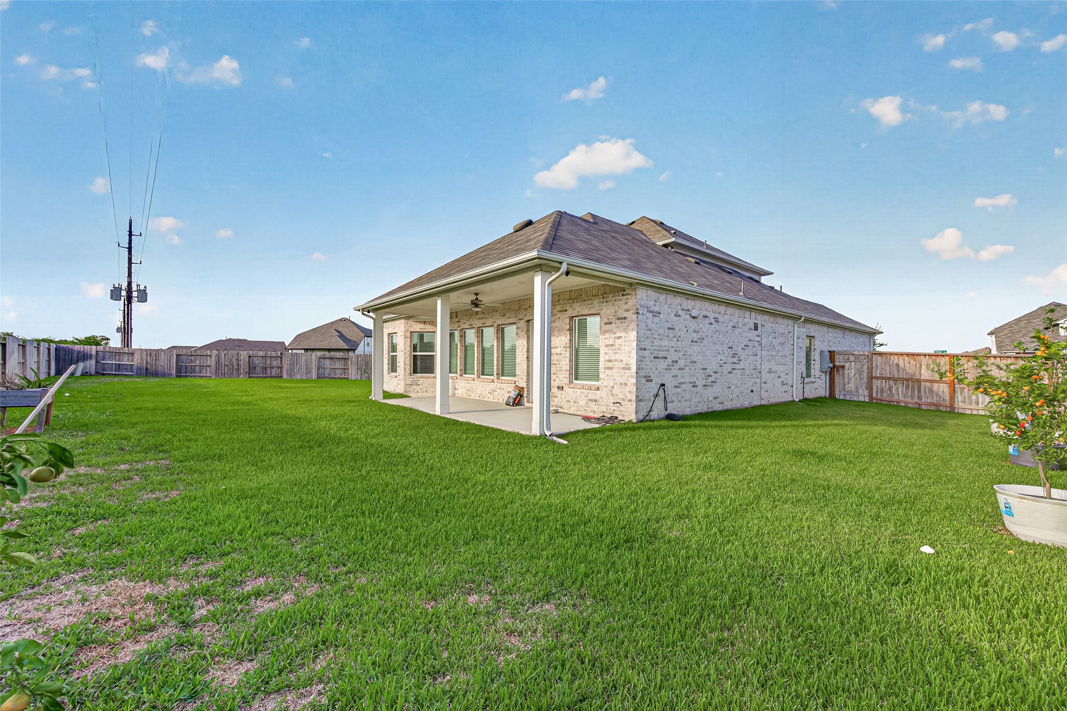 Backyard view showing the covered patio and large grassy yard with wood privacy fence.