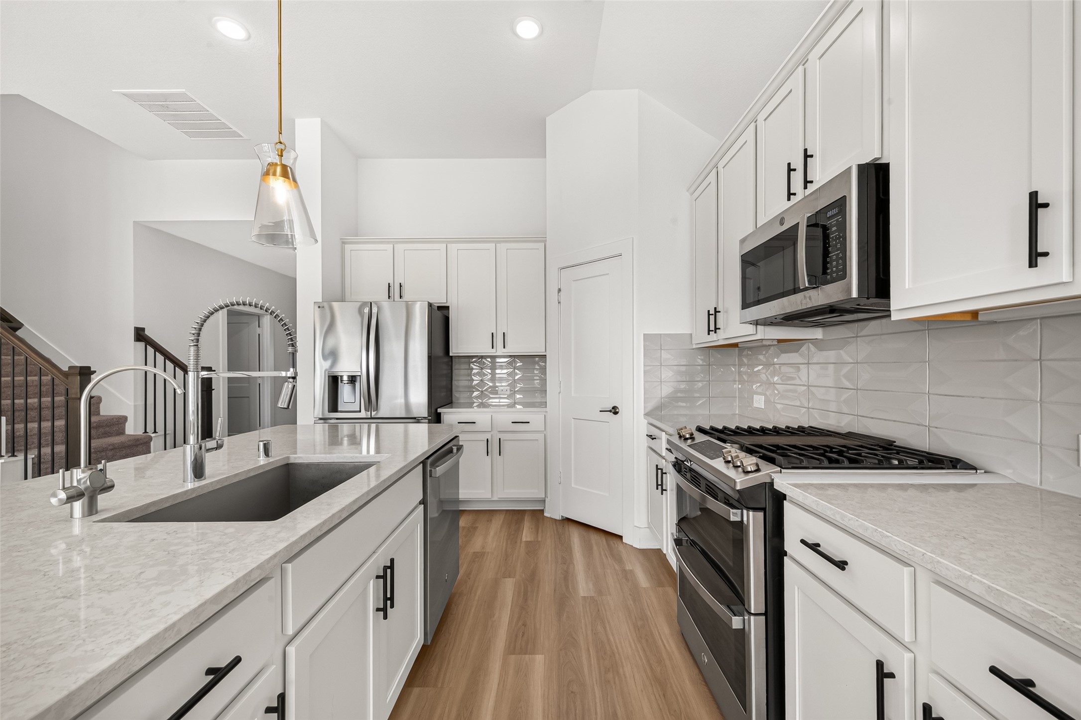 Kitchen with gas range, stainless steel appliances, ample counter space, and white cabinets with black hardware.