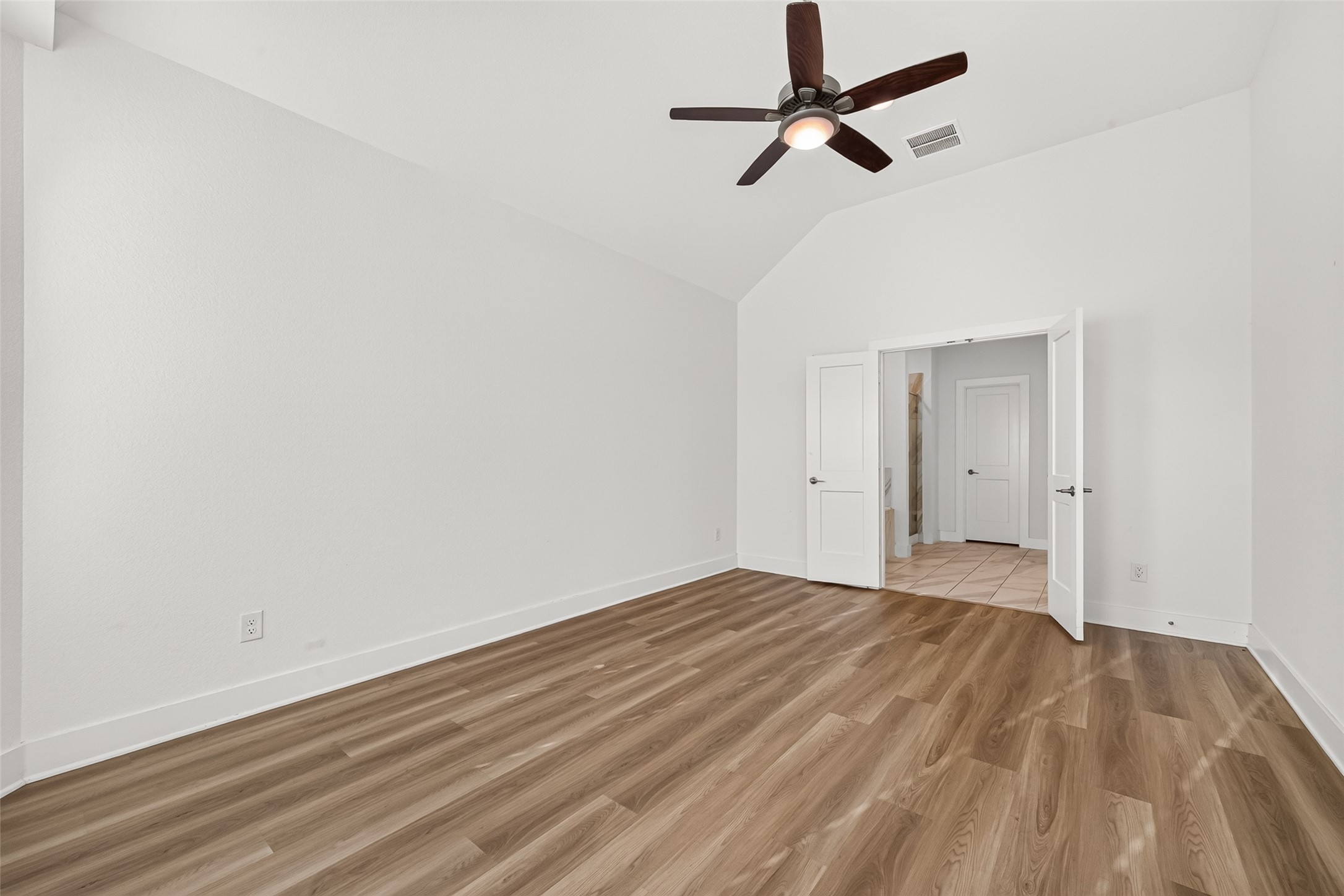 Primary bedroom with vaulted ceiling, ceiling fan, and double-door entry.