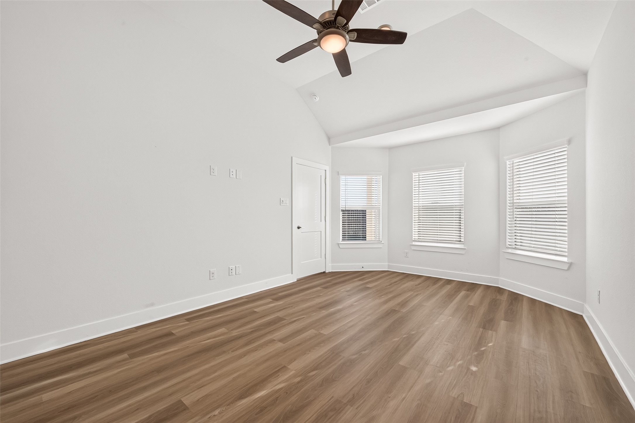 Primary bedroom with bay window, vaulted ceiling, ceiling fan, and wood-look flooring.