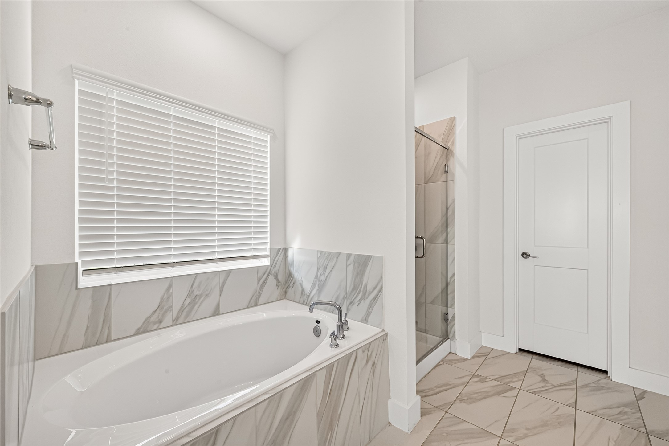 Primary bathroom with soaking tub, marble-look tile surround, and separate shower.