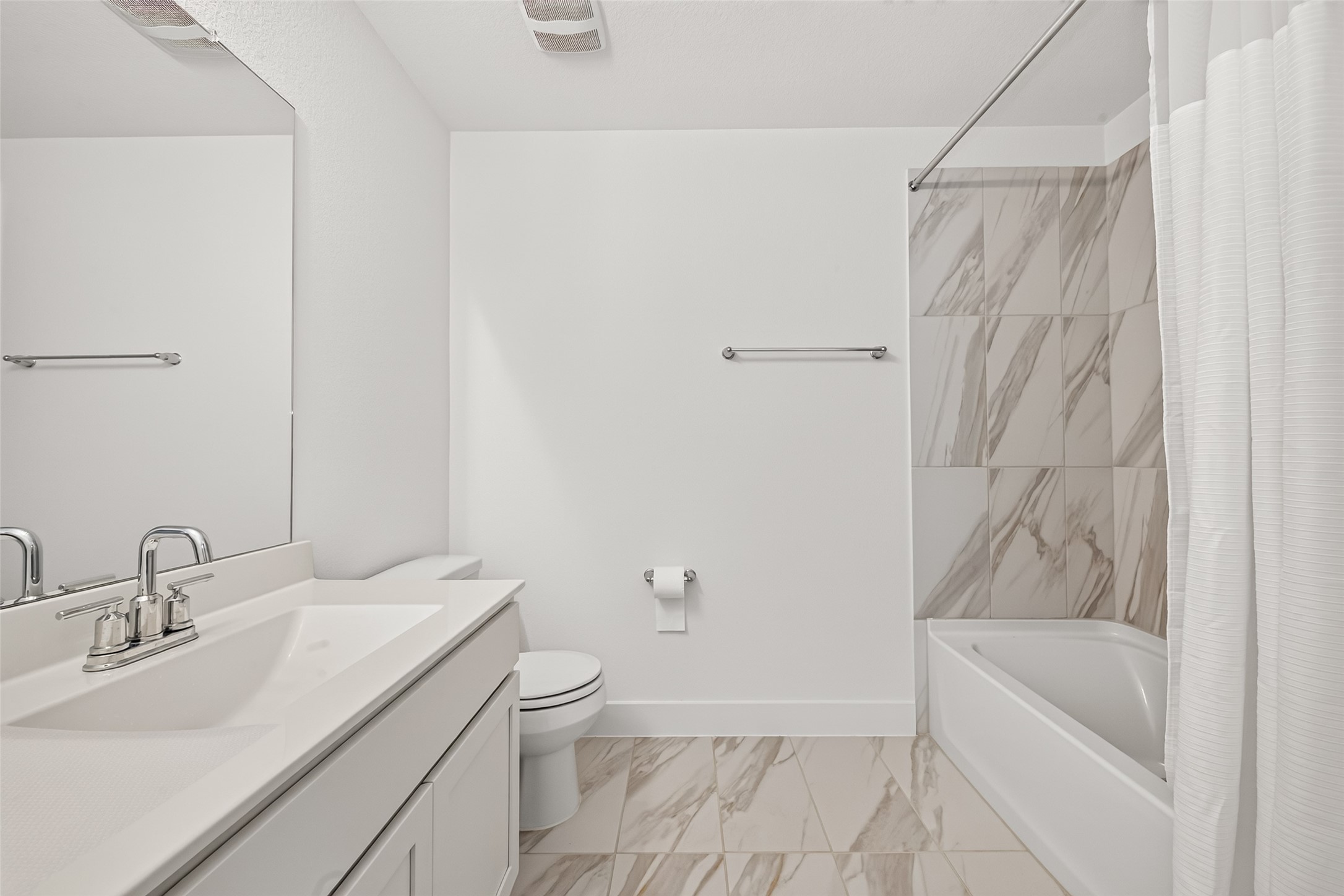Secondary bathroom with tub/shower combination, marble-look tile surround, and tile flooring.