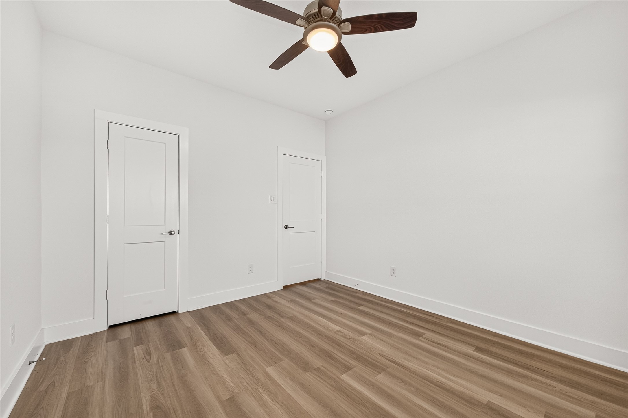 Bedroom view showing closet doors, ceiling fan, and wood-look flooring.