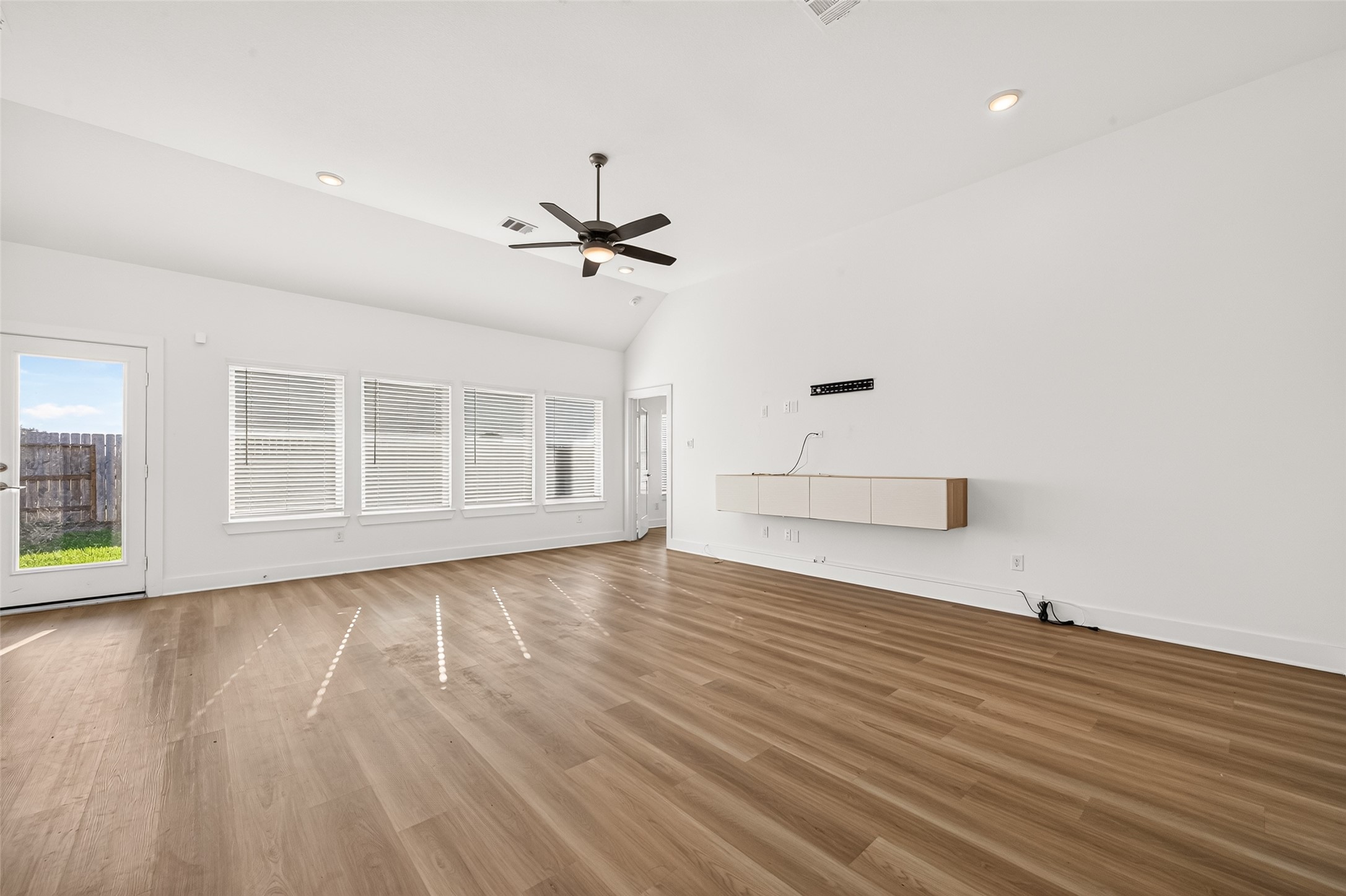 Living room with high ceiling, ceiling fan, recessed lighting, and a wall of windows with door access to the backyard. Living room with high ceiling, ceiling fan, recessed lighting, and a wall of windows with door access to the backyard.