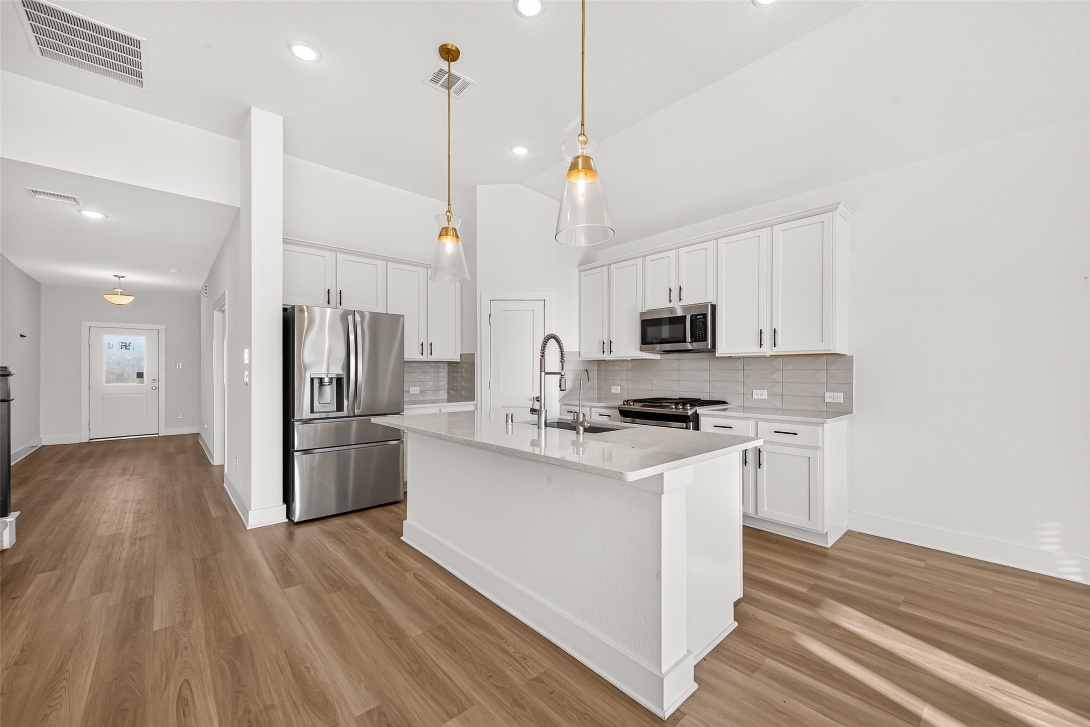 Kitchen with large island, gas range, stainless steel appliances, tile backsplash, and pendant lights.