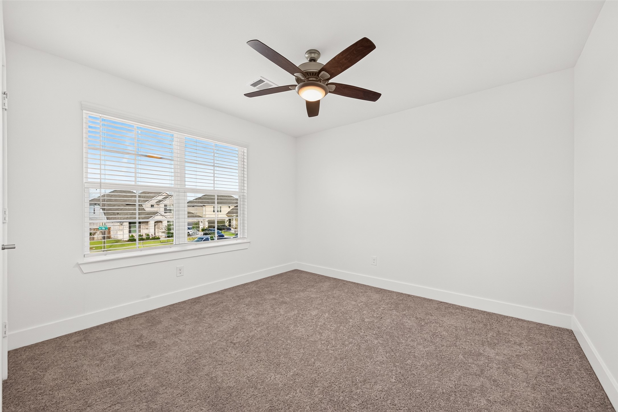 Upstairs bedroom with carpet, ceiling fan, and window with blinds.