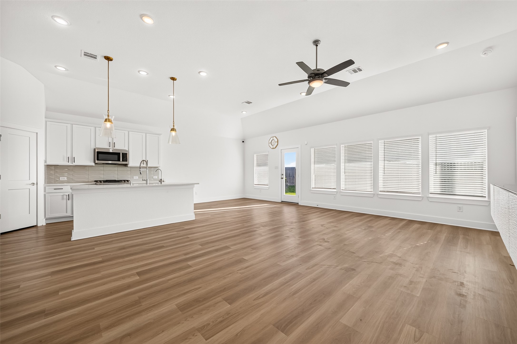 Open-concept layout with the living room flowing into the kitchen and breakfast area, with large windows and wood-look flooring.