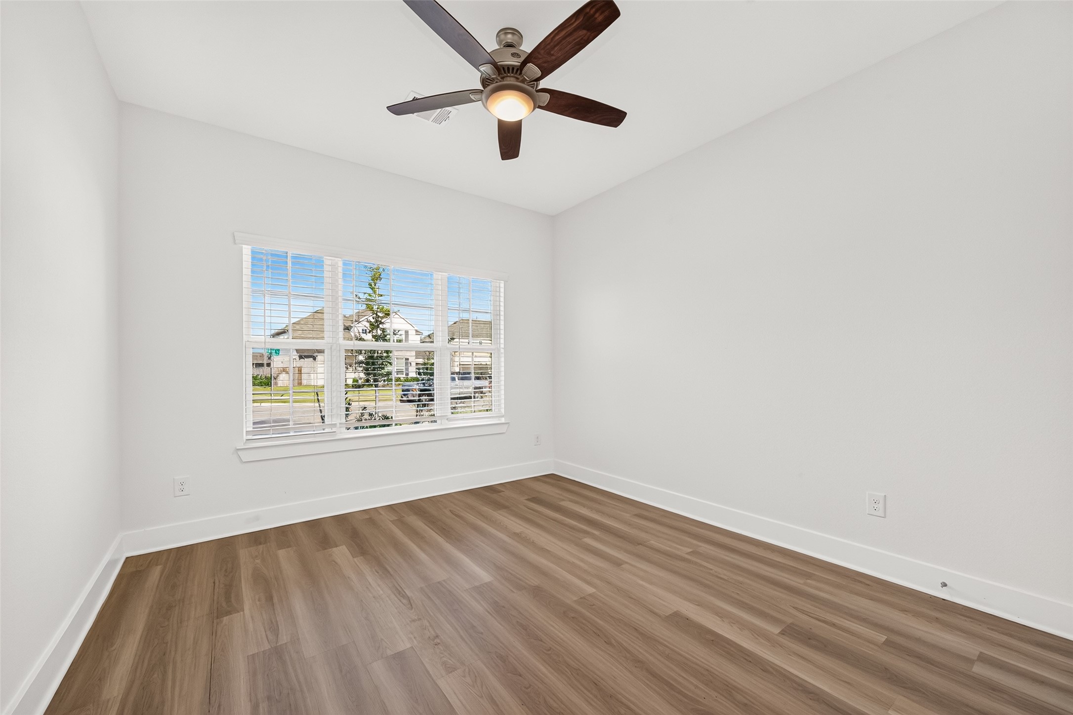 Bedroom with ceiling fan, wood-look flooring, and a front-facing window.