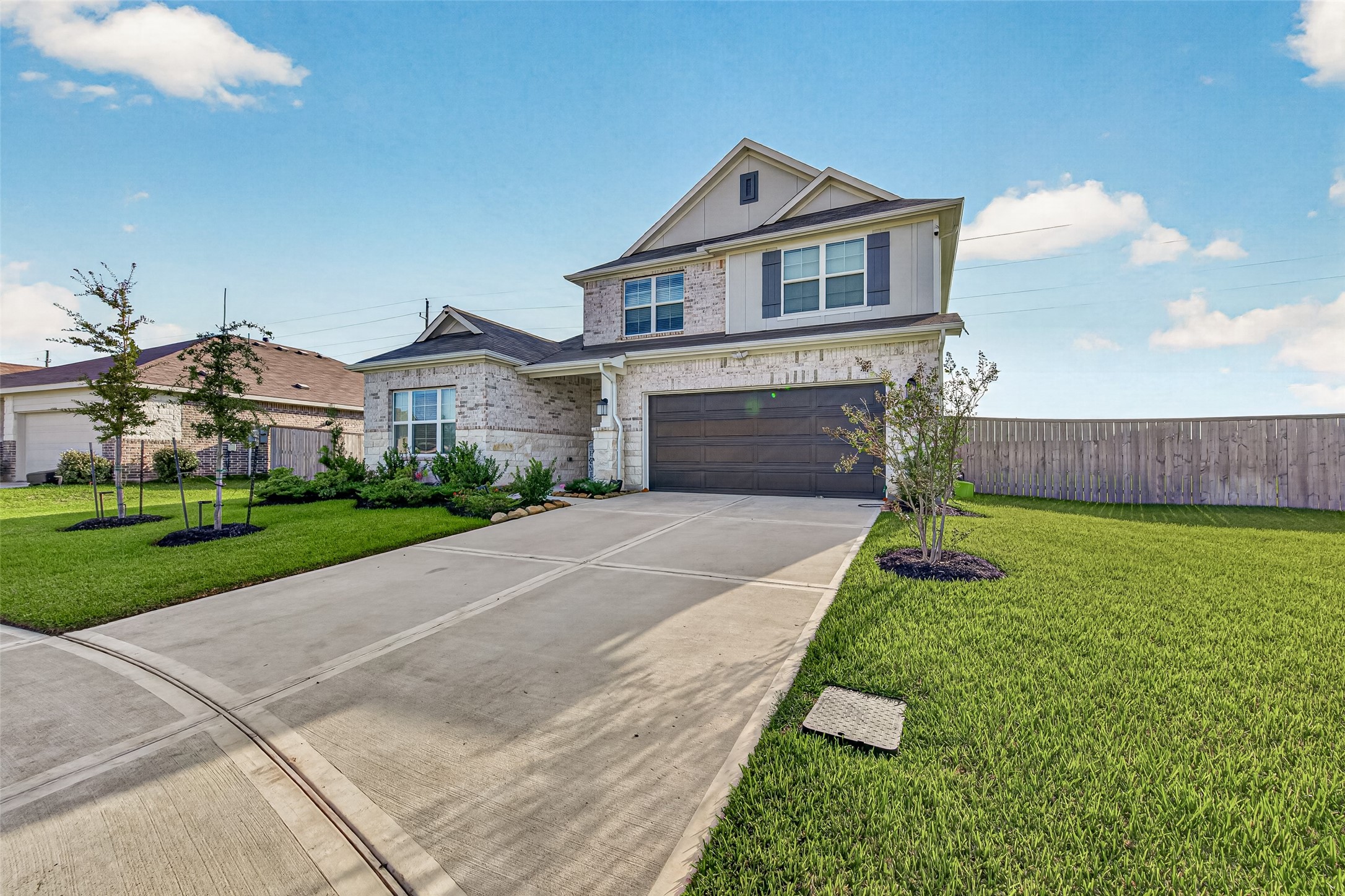Two-story brick and stone home with a two-car garage, long driveway, and landscaped front lawn.