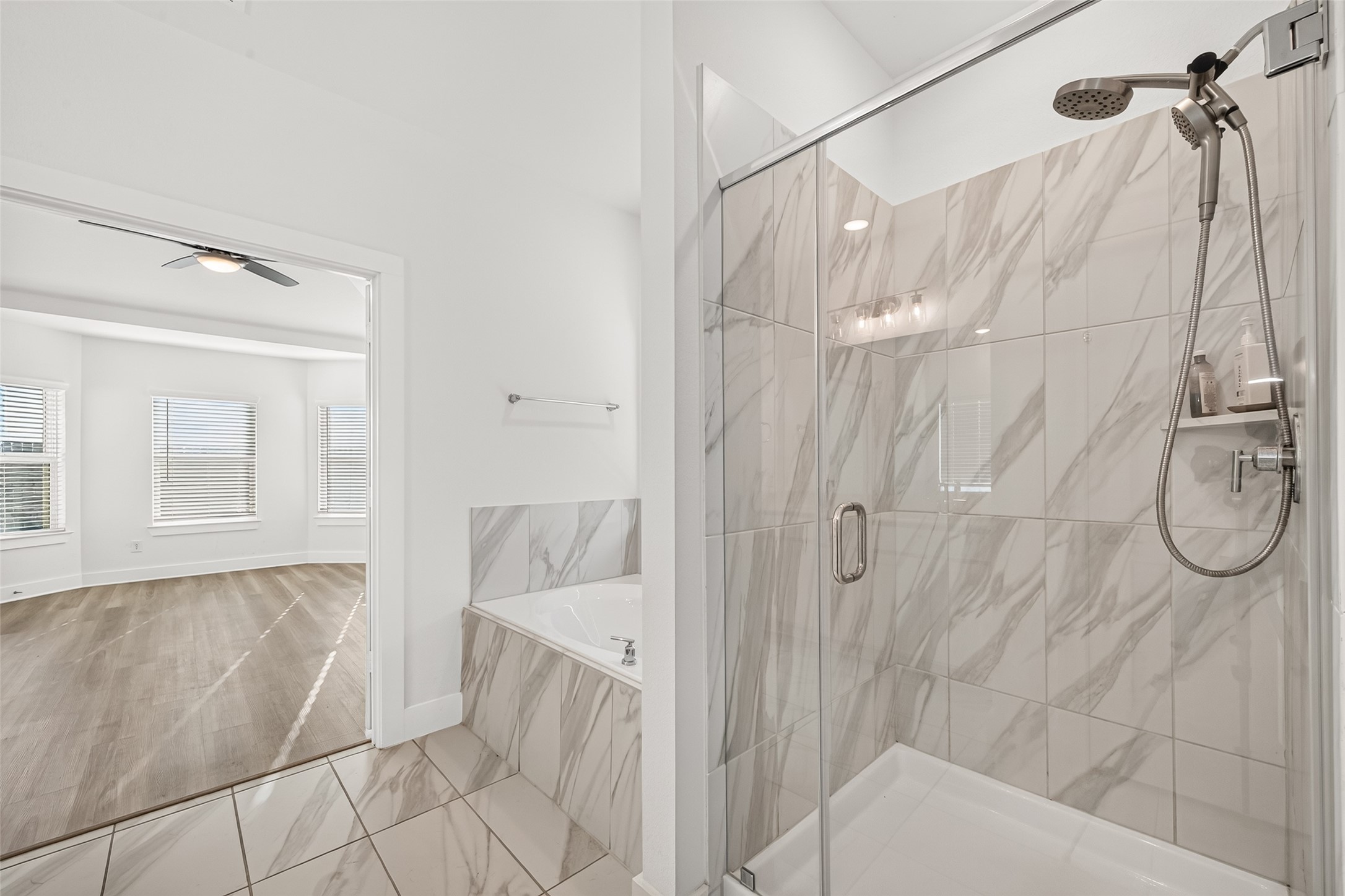 Walk-in shower with frameless glass enclosure, handheld showerhead, and marble-look tile.