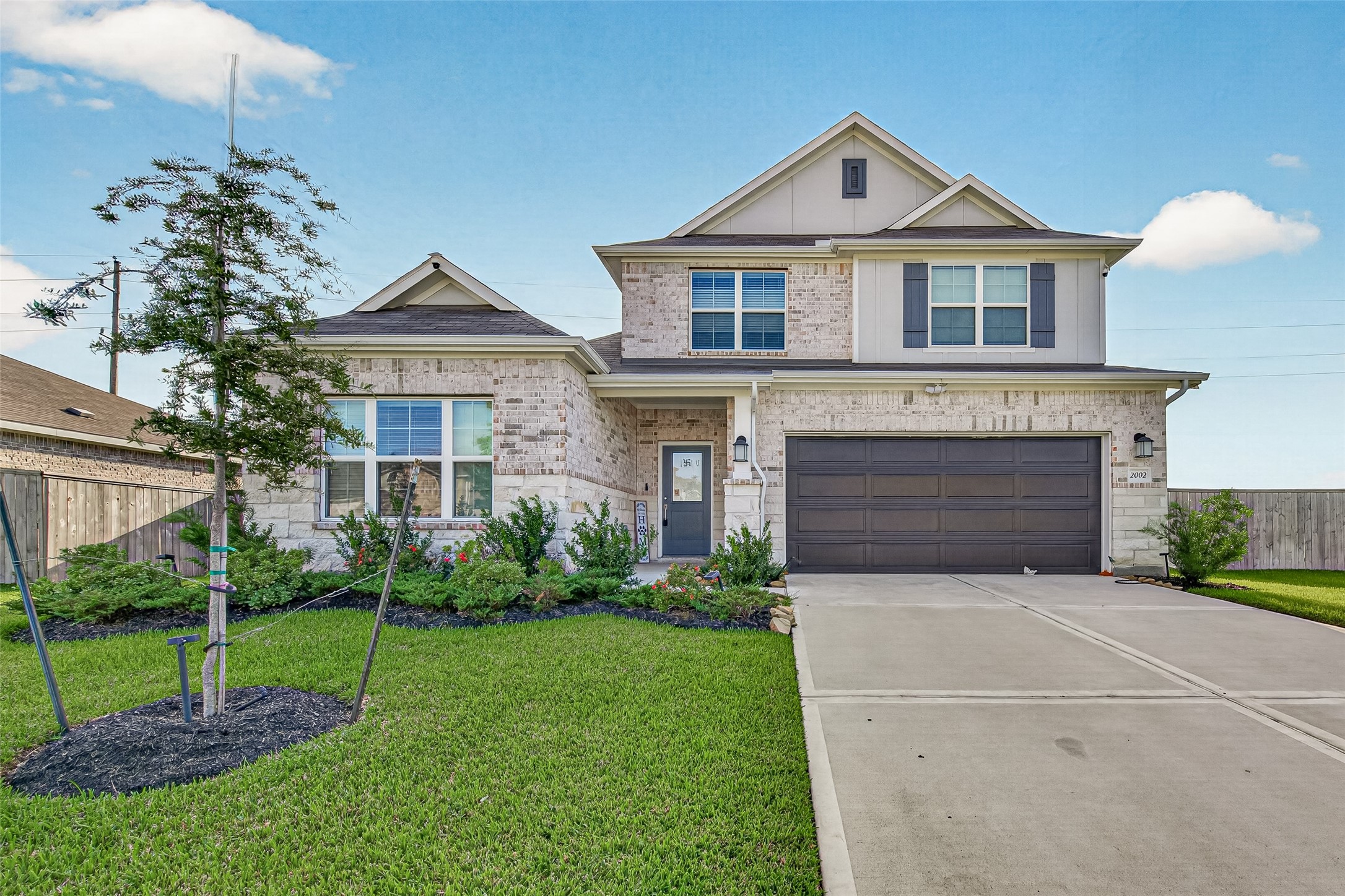 Front exterior with landscaped lawn, young shade tree, and wide driveway.