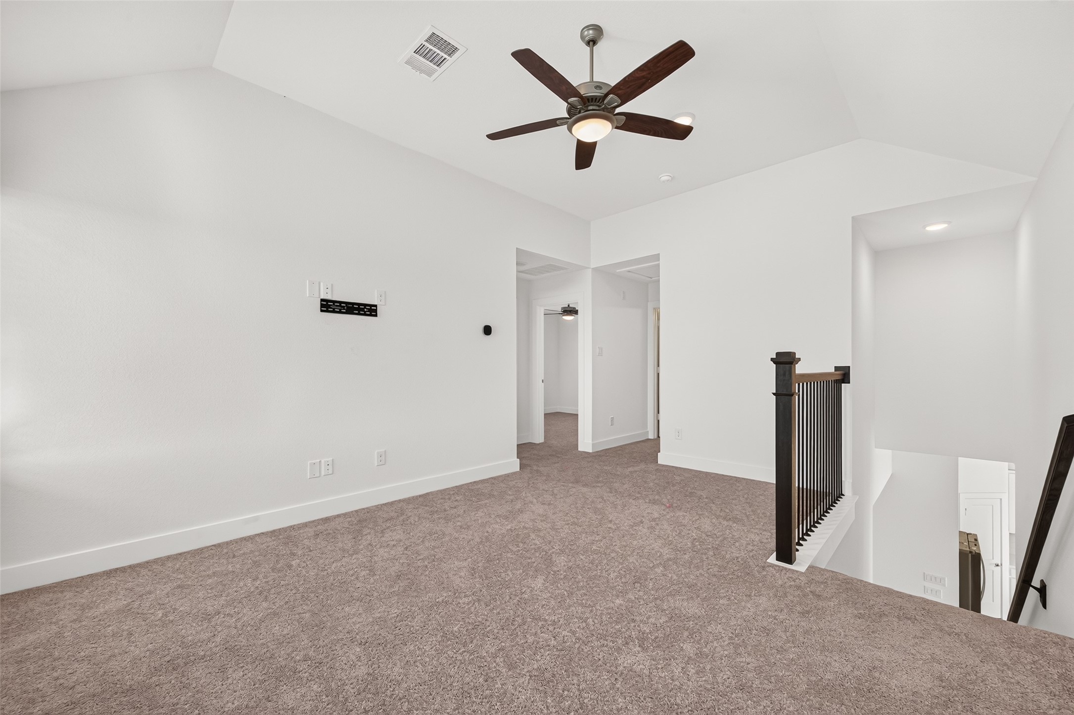 Upstairs loft/game room with carpet, ceiling fan, and stair railing.