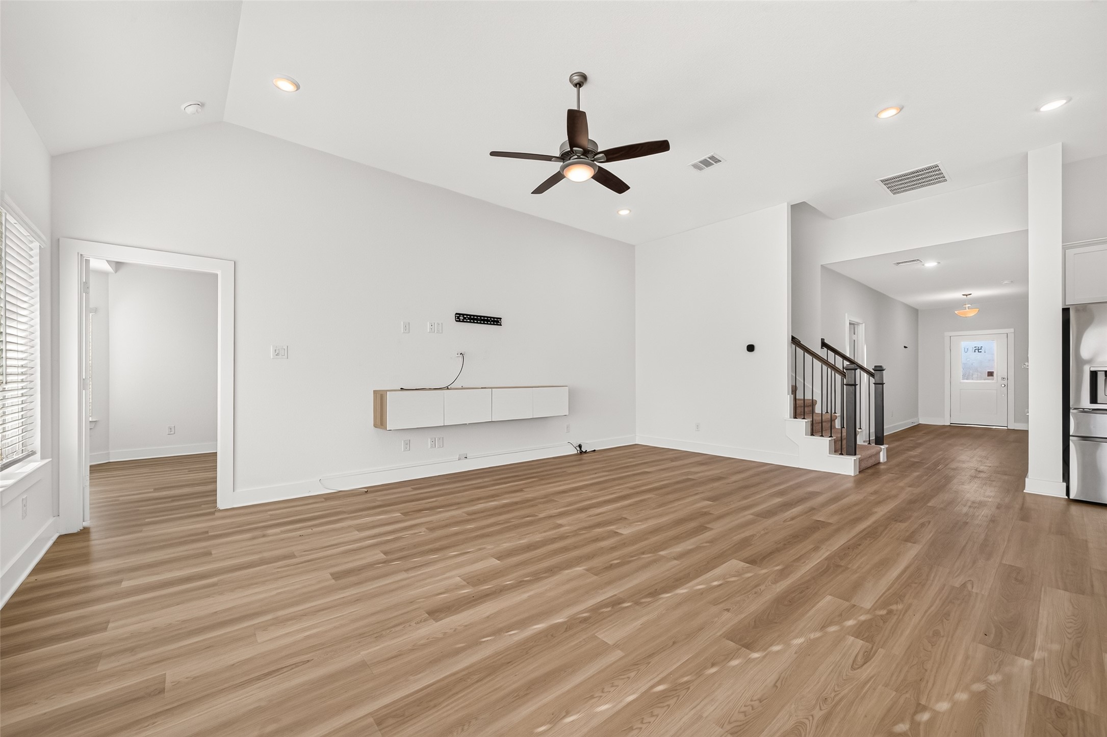 Living room with vaulted ceiling and ceiling fan, open to the hallway, staircase, and kitchen.