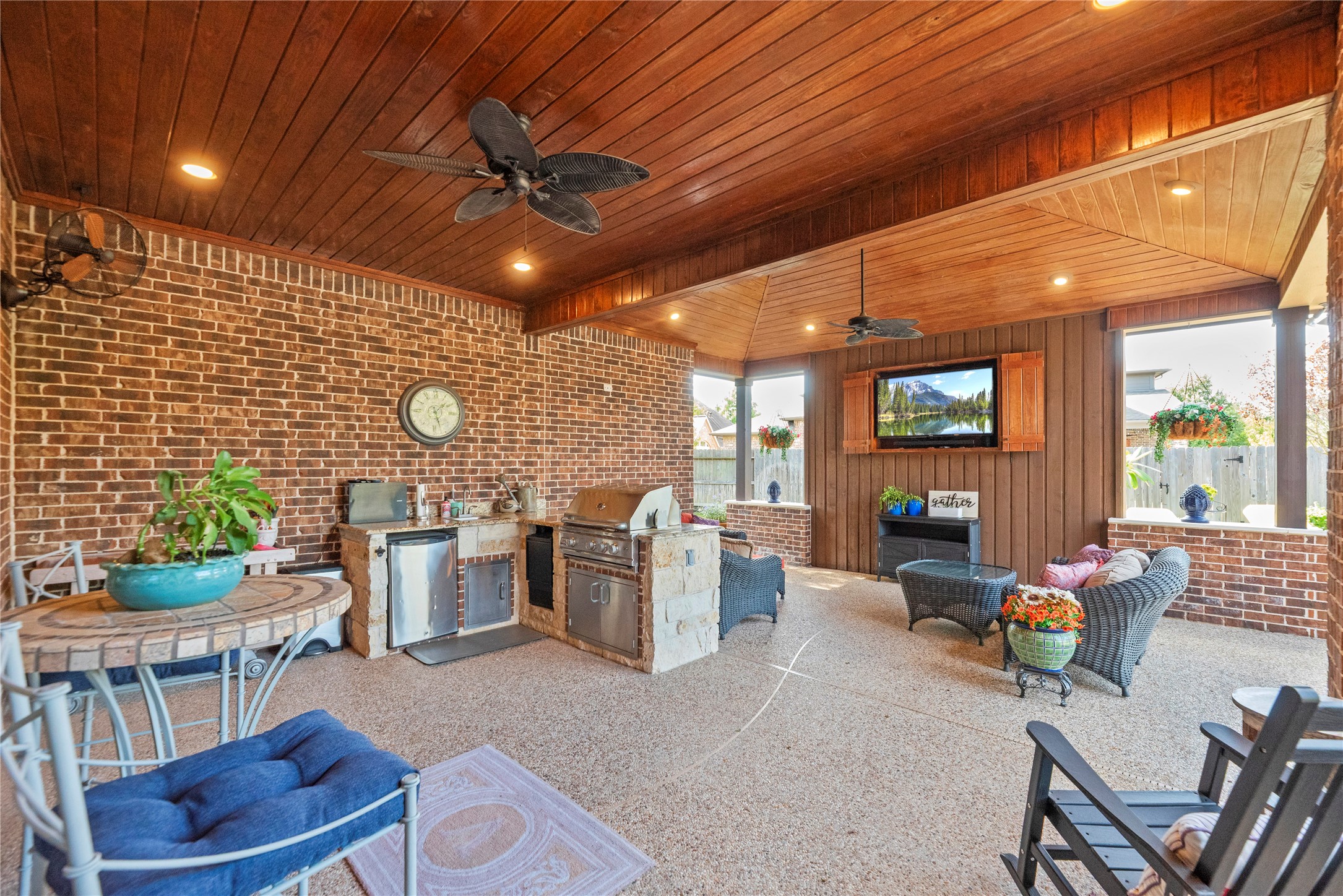Spacious covered outdoor living area featuring a wood-paneled ceiling, ceiling fans, and plenty of room for entertaining.