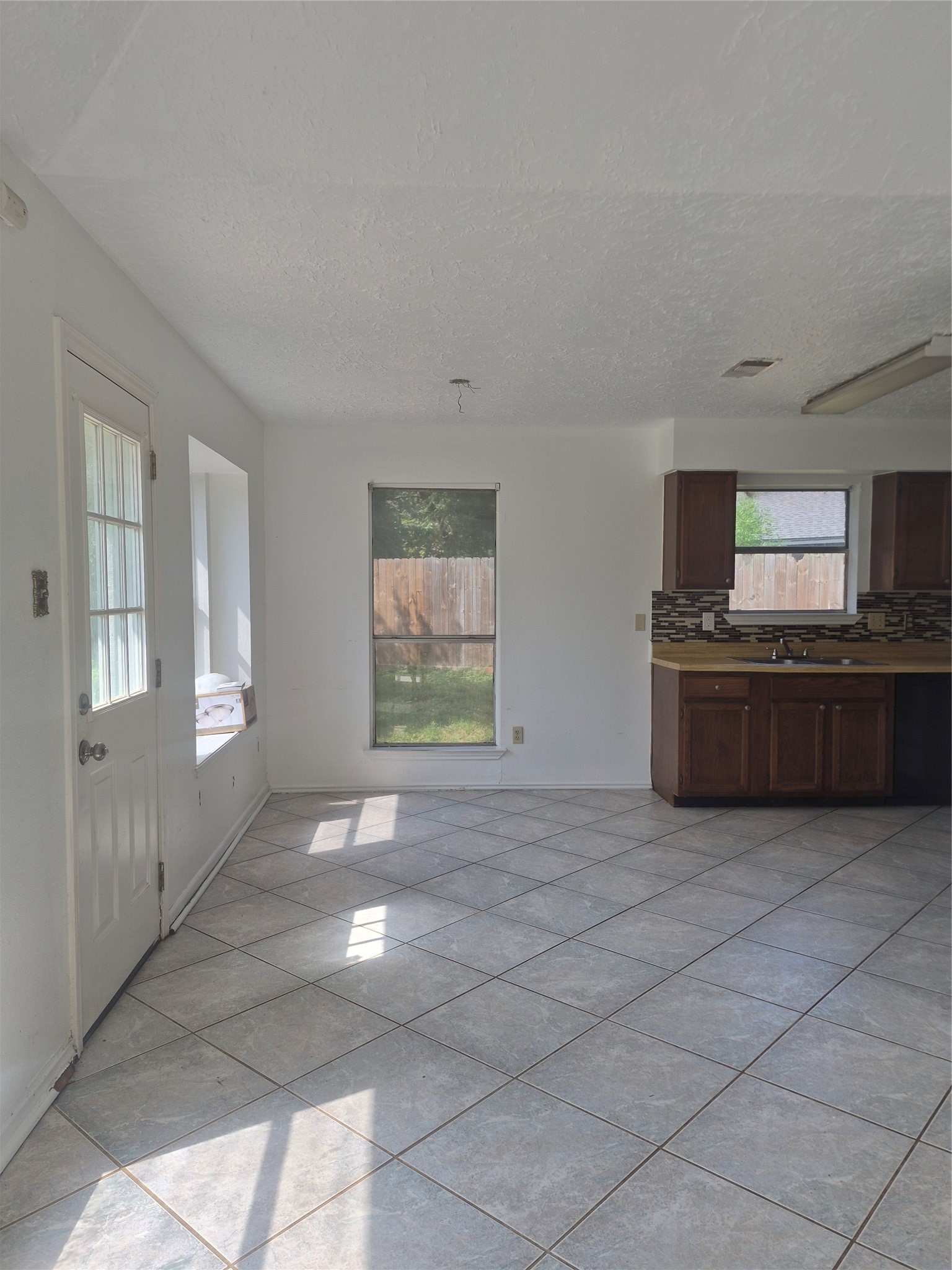 Kitchen with large windows, tile flooring, offering a view of the backyard.