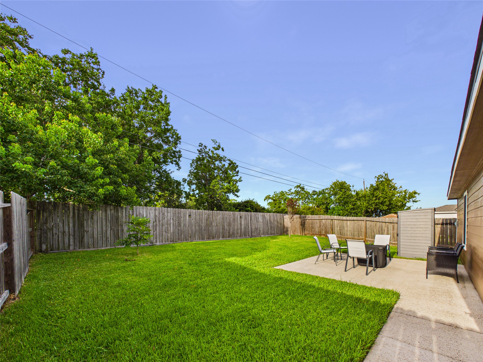 Spacious backyard with lush green lawn, a cozy patio area for outdoor dining, and a privacy fence, perfect for relaxation and entertainment.