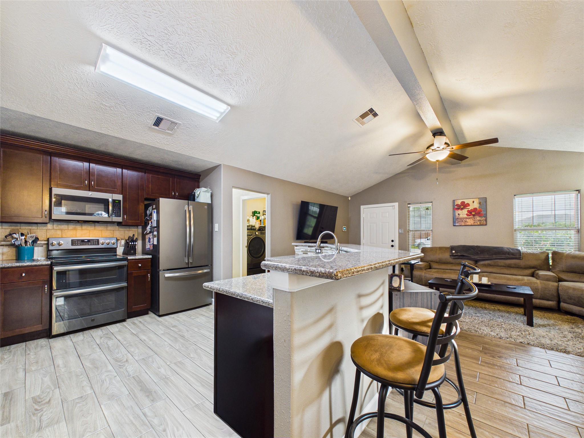 The kitchen features stainless steel appliances, dark wood cabinetry, and a breakfast bar overlooking the living.