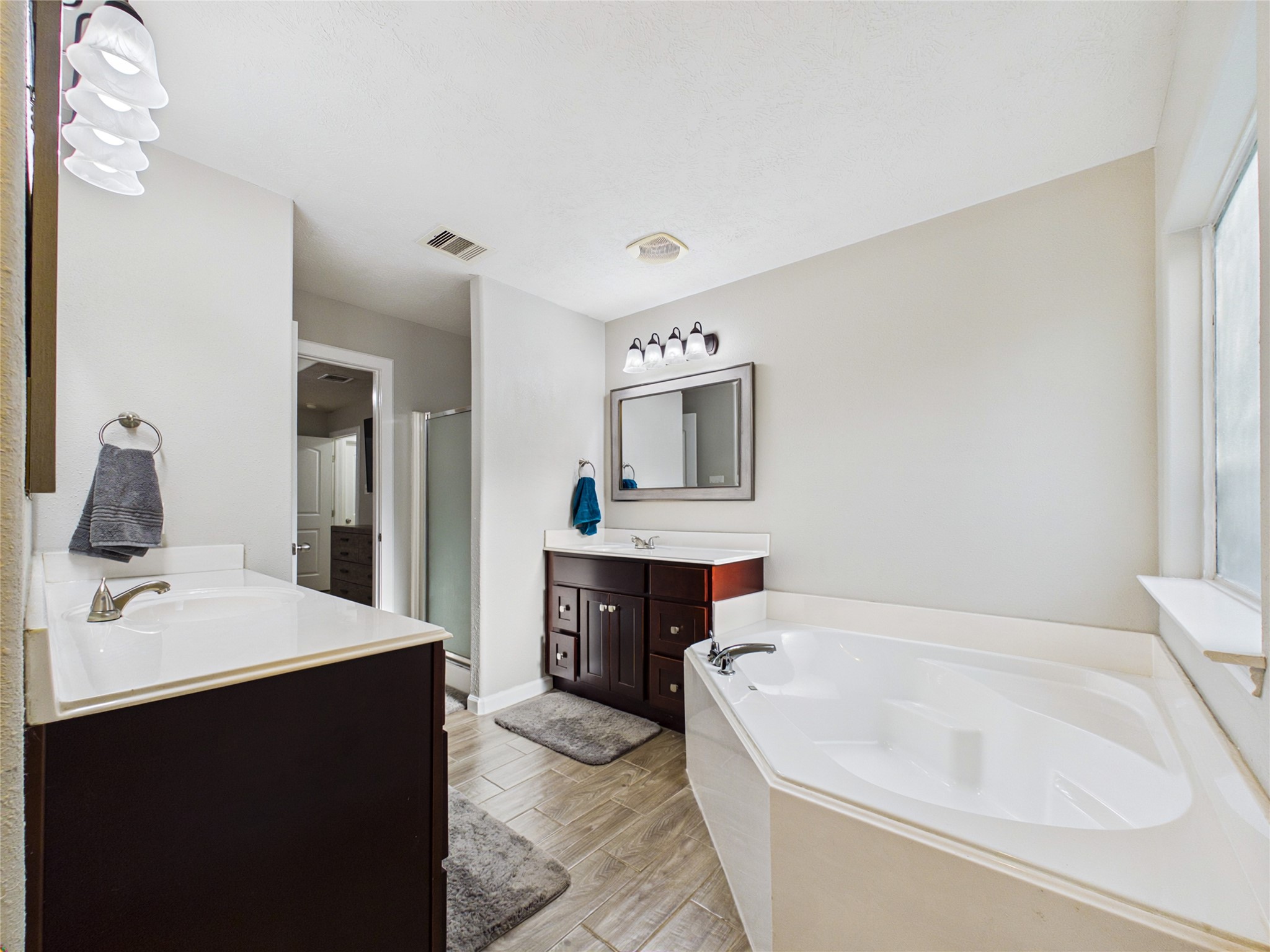 Primary bathroom featuring his-and-hers vanities, a spacious soaking tub, and a separate shower.