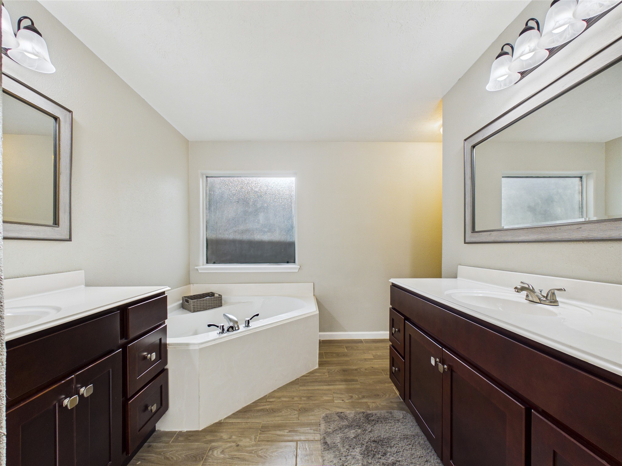 Primary bathroom featuring his-and-hers vanities, a spacious soaking tub, and a separate shower.