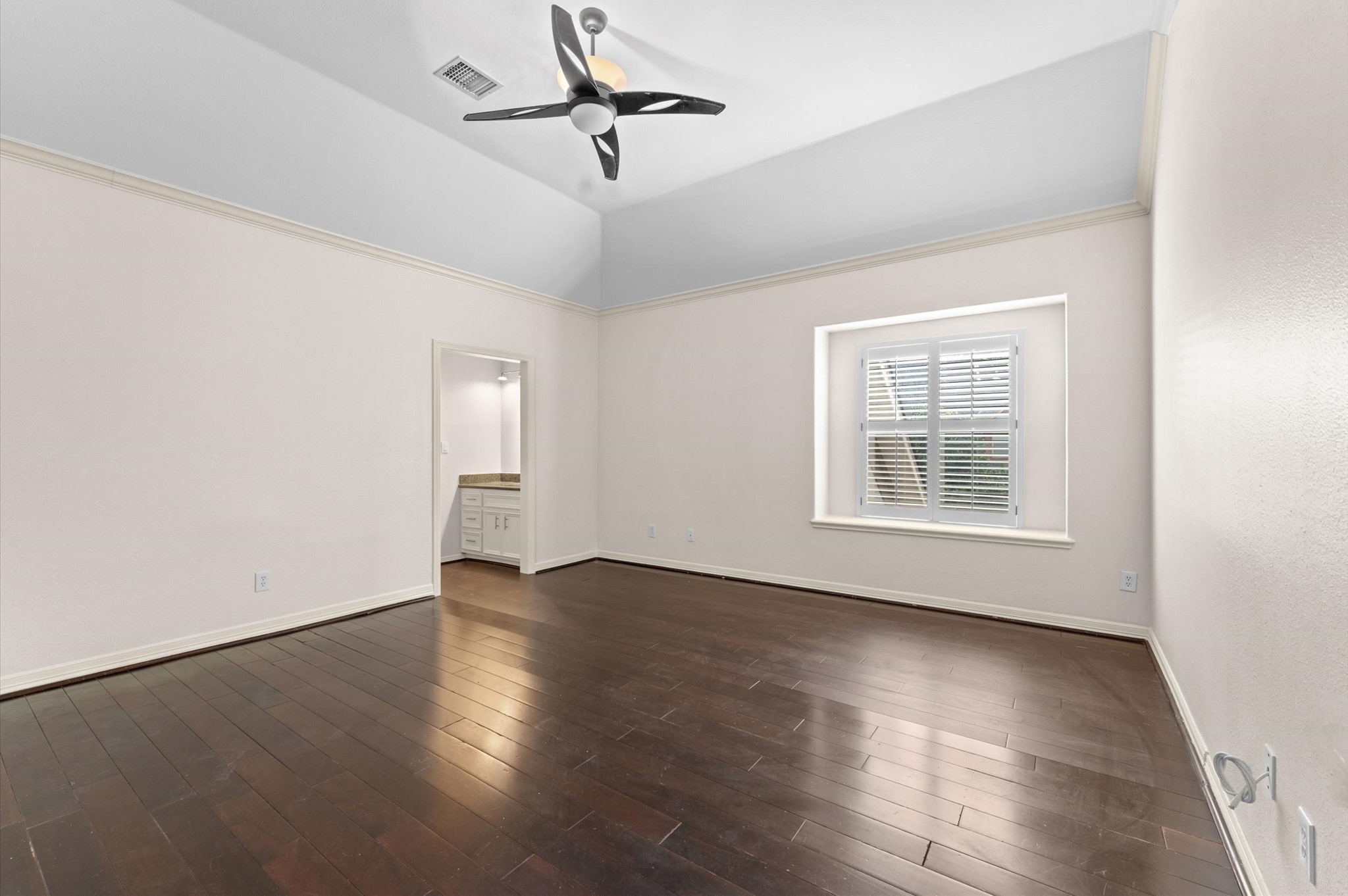 This bedroom has beautiful wood flooring. At the corner you see the sink into the bathroom area.