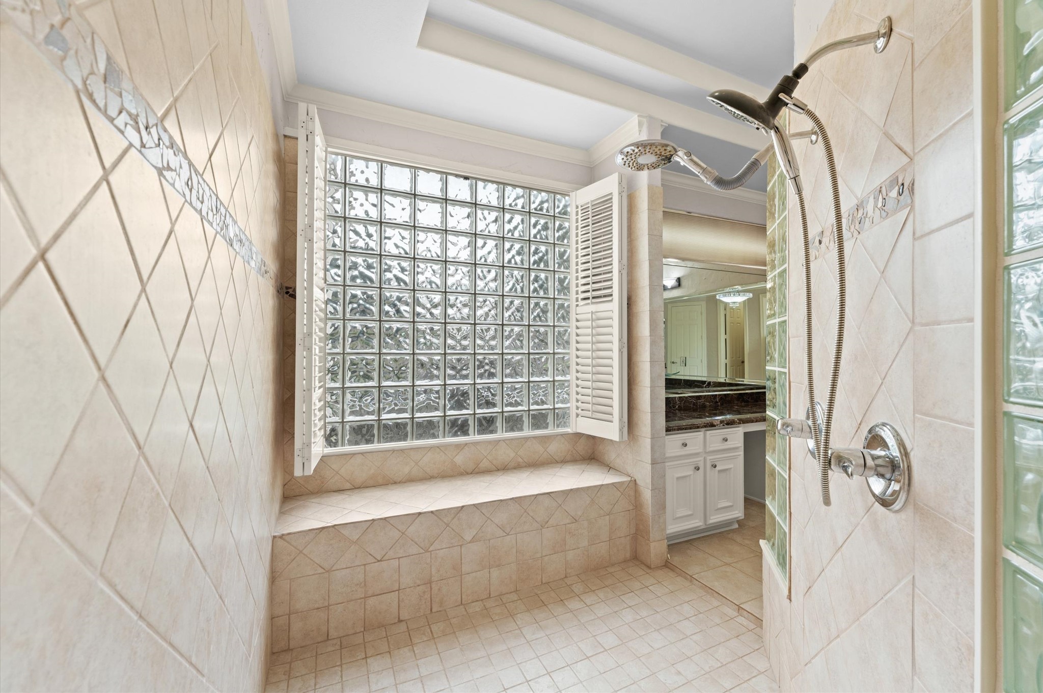A view of the walk-through shower has multiple shower heads and large glass block window with shower bench.