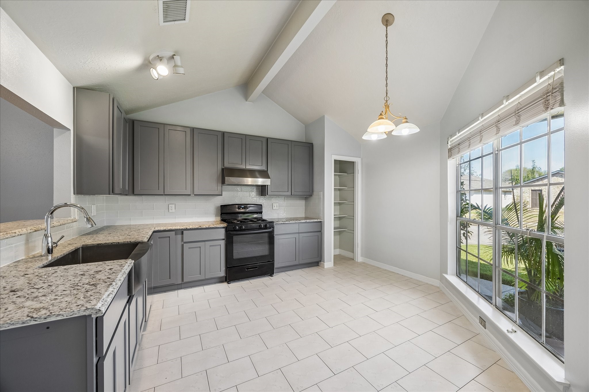 Remodeled kitchen features granite countertops, updated millwork cabinetry, stainless appliances, a vented range hood, and tile flooring. Large windows brighten the adjoining breakfast area.
