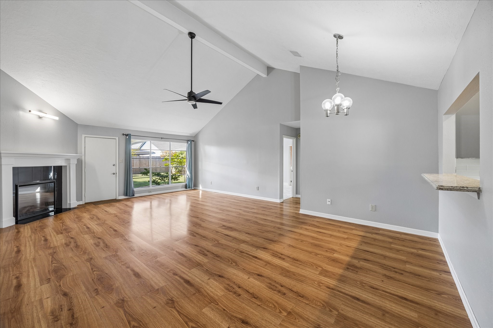 Wide-angle view highlights the open relationship between the living and dining areas beneath the high ceiling and exposed beam, with clear sightlines toward the backyard.