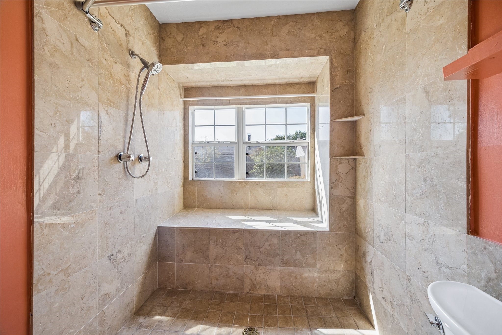 Generously sized tiled shower features a handheld fixture, built-in ledge, and window that brings natural light into the primary bath.