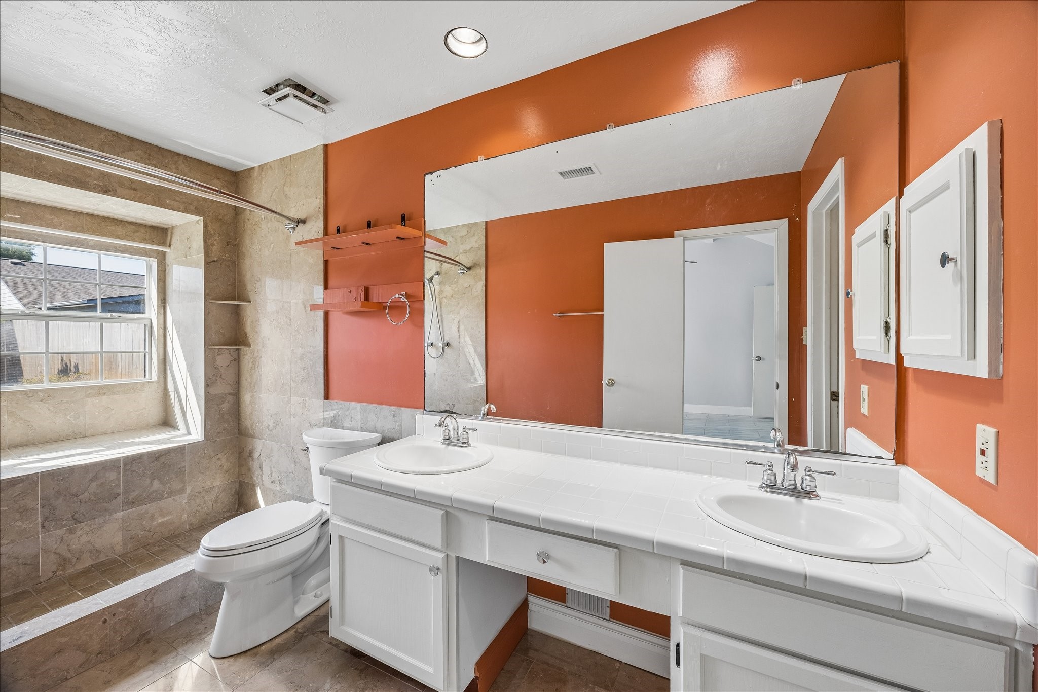 Primary bath offers a long dual-sink vanity, broad mirror, tiled finishes, and a warm accent wall that adds character to the space.