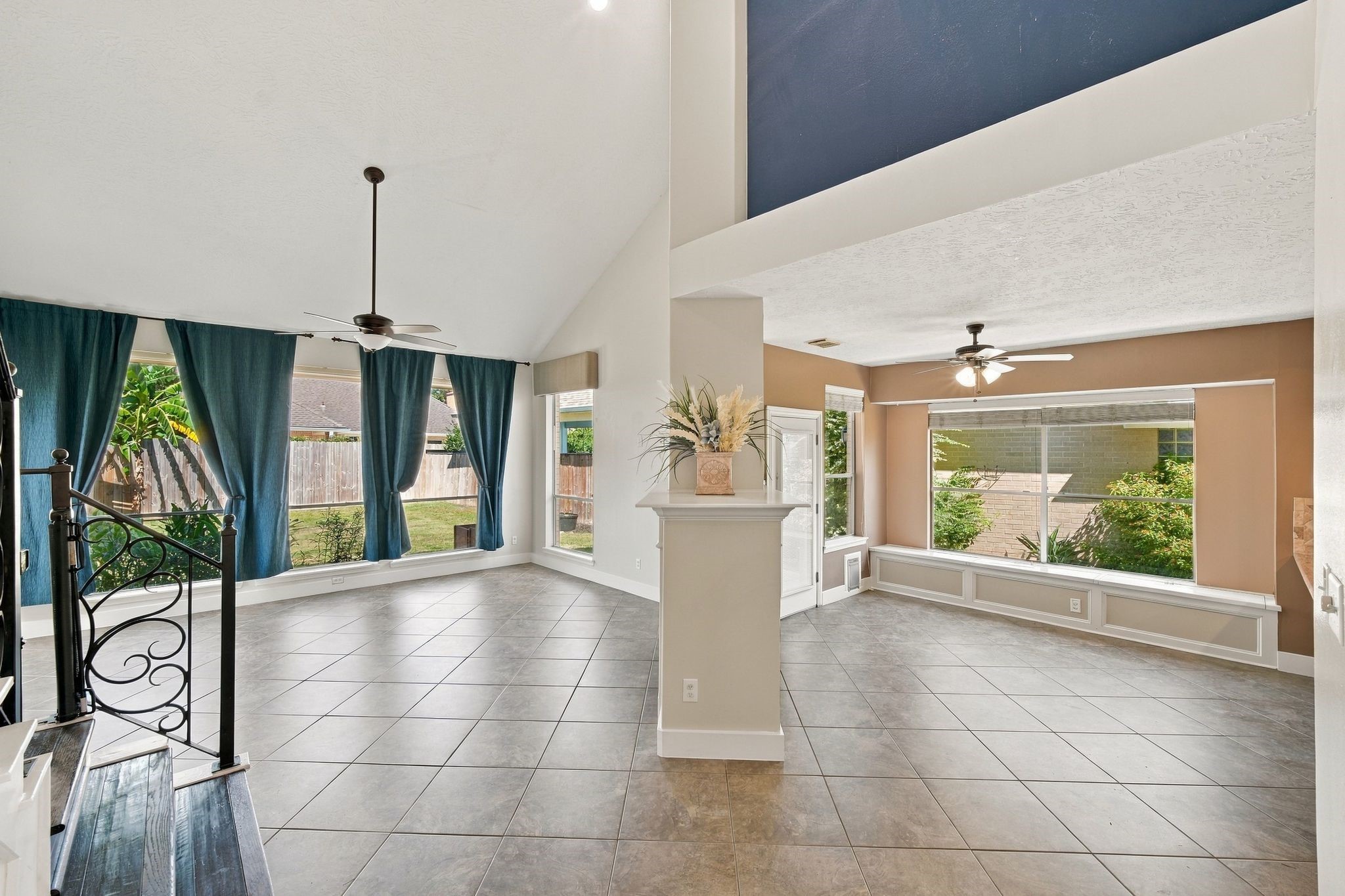 Spacious and filled with natural light, this versatile, unstaged living area features high ceilings, elegant tile flooring, and large windows overlooking lush greenery, offering a perfect canvas for your personal touch.