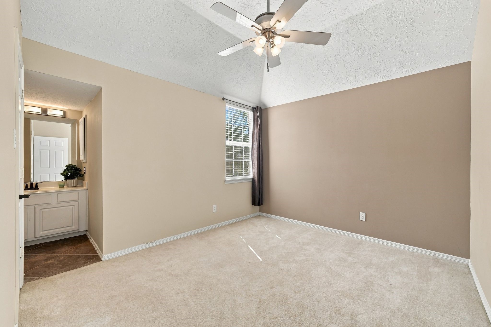 Discover the potential of this unstaged room featuring a vaulted ceiling, soft carpet, and ample natural light, leading to a cozy en-suite bathroom.