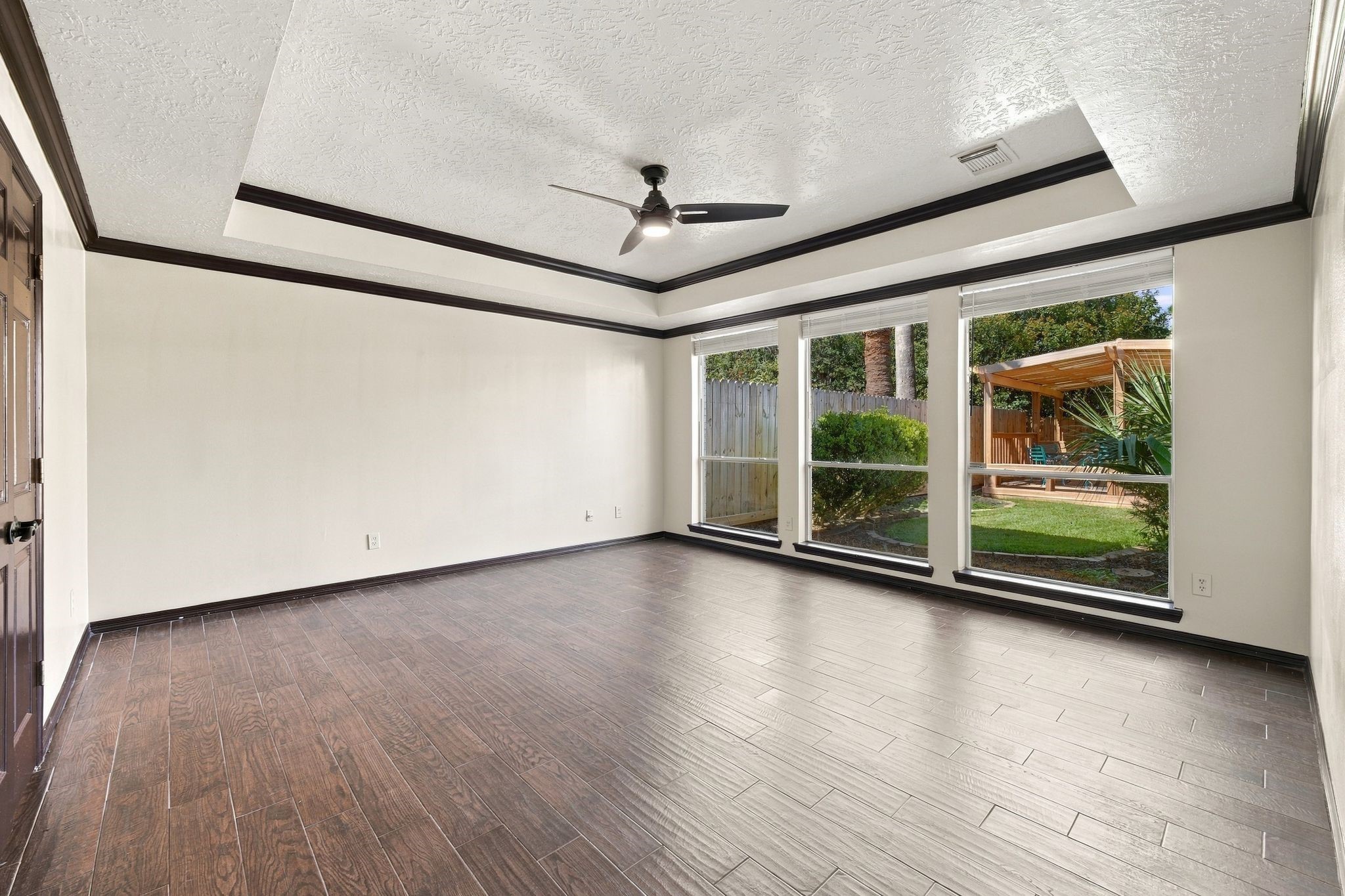 Discover the potential in this unstaged room, featuring elegant wood flooring, a modern ceiling fan, and expansive windows that offer a serene view of the lush backyard oasis.