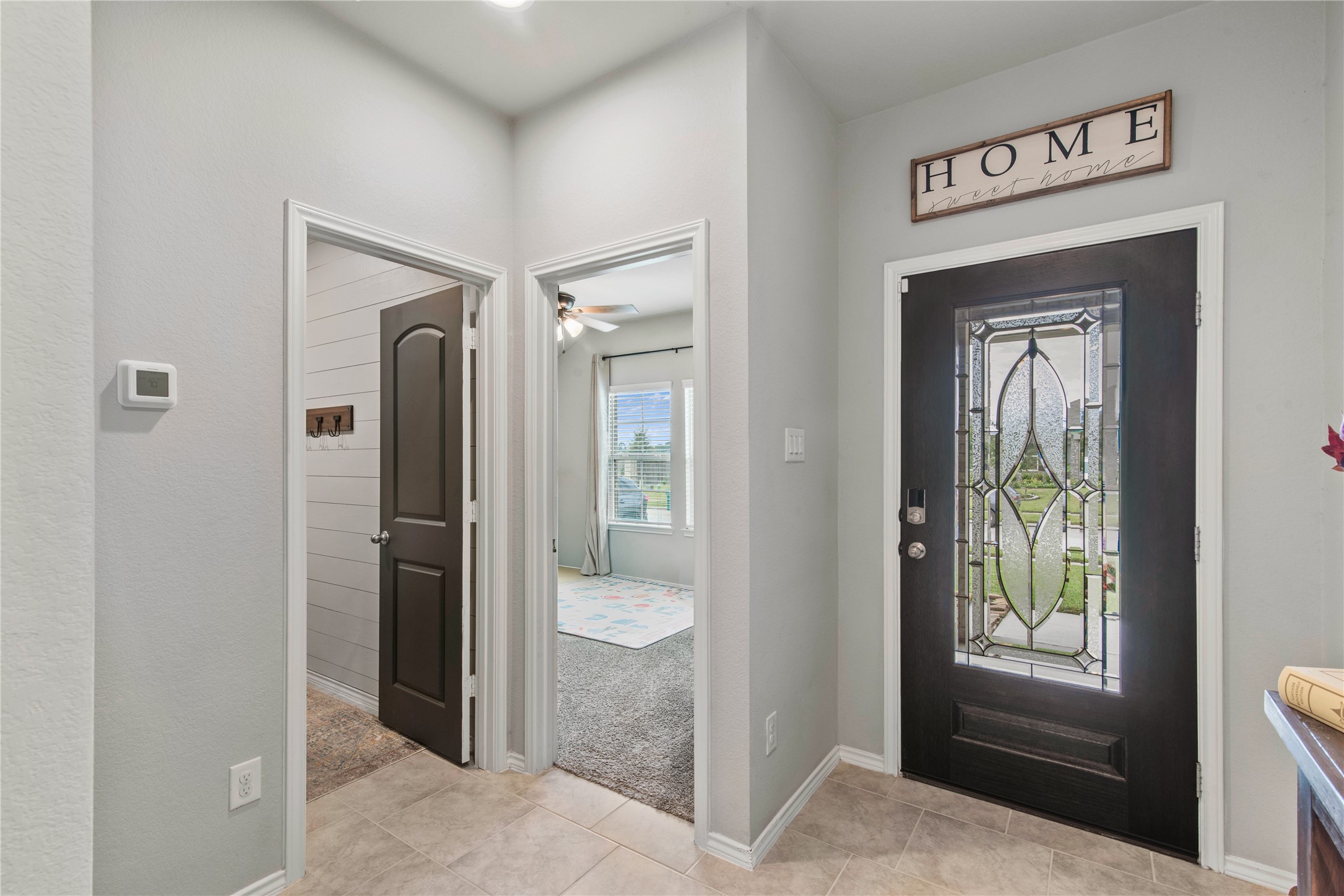 Inviting entryway features a decorative glass front door, neutral tile flooring, and access to cozy rooms with soft carpeting and natural light.
