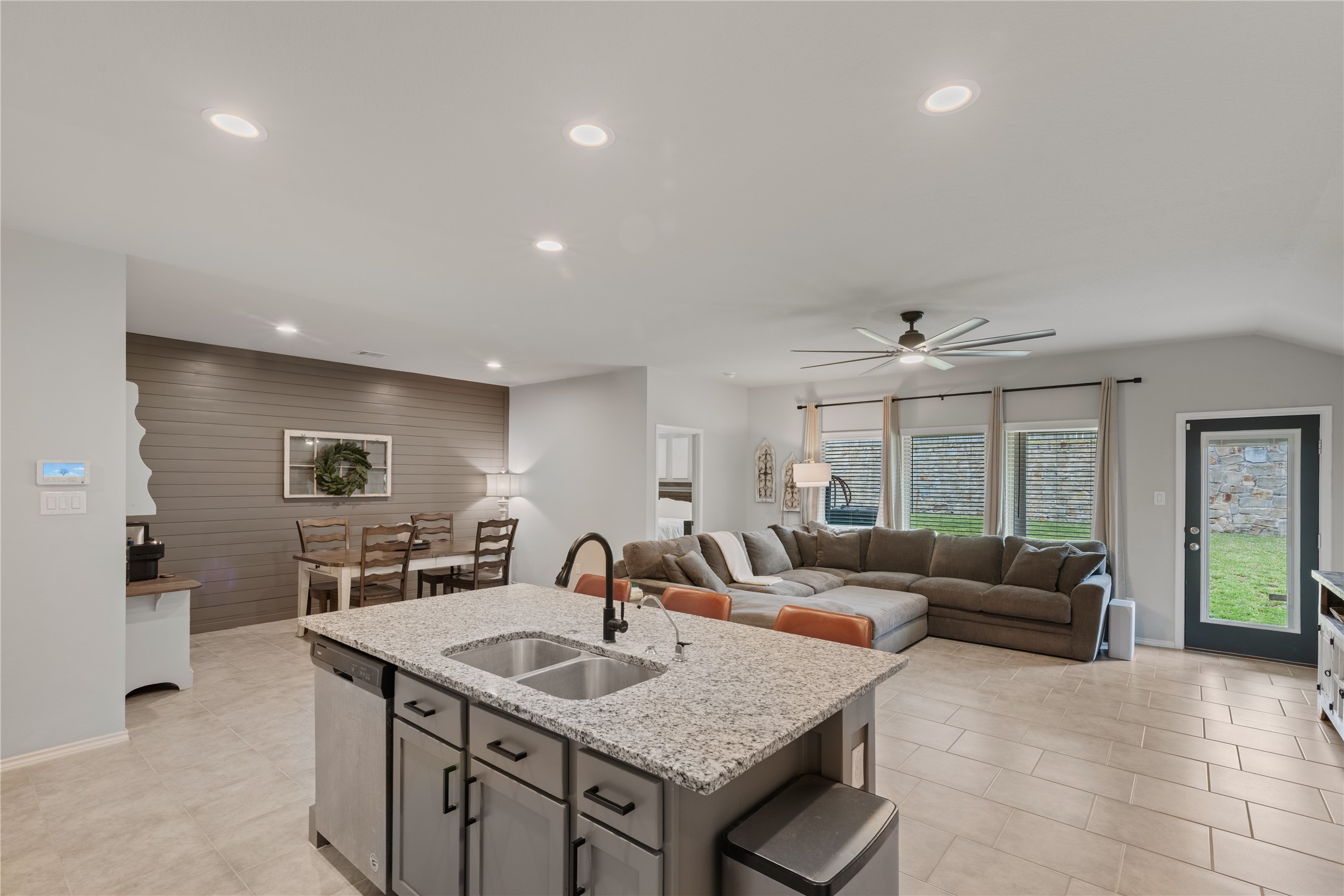 Spacious open-concept living area features a modern kitchen with granite countertops and a large island, seamlessly flowing into a cozy living room with ample seating and natural light from multiple windows.