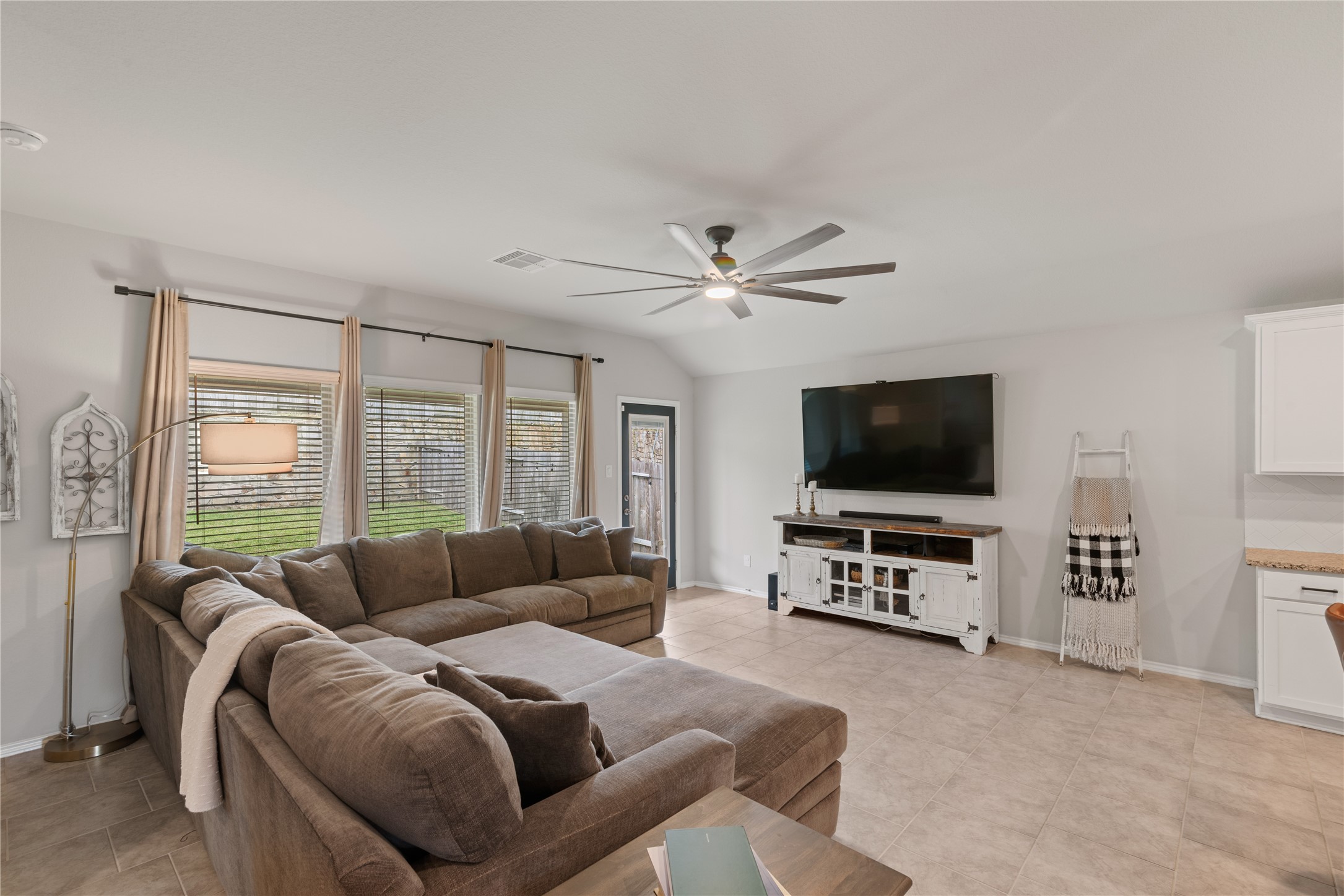 Spacious living room featuring a cozy sectional sofa, large windows with natural light, and a sleek ceiling fan, perfect for relaxation and entertainment.