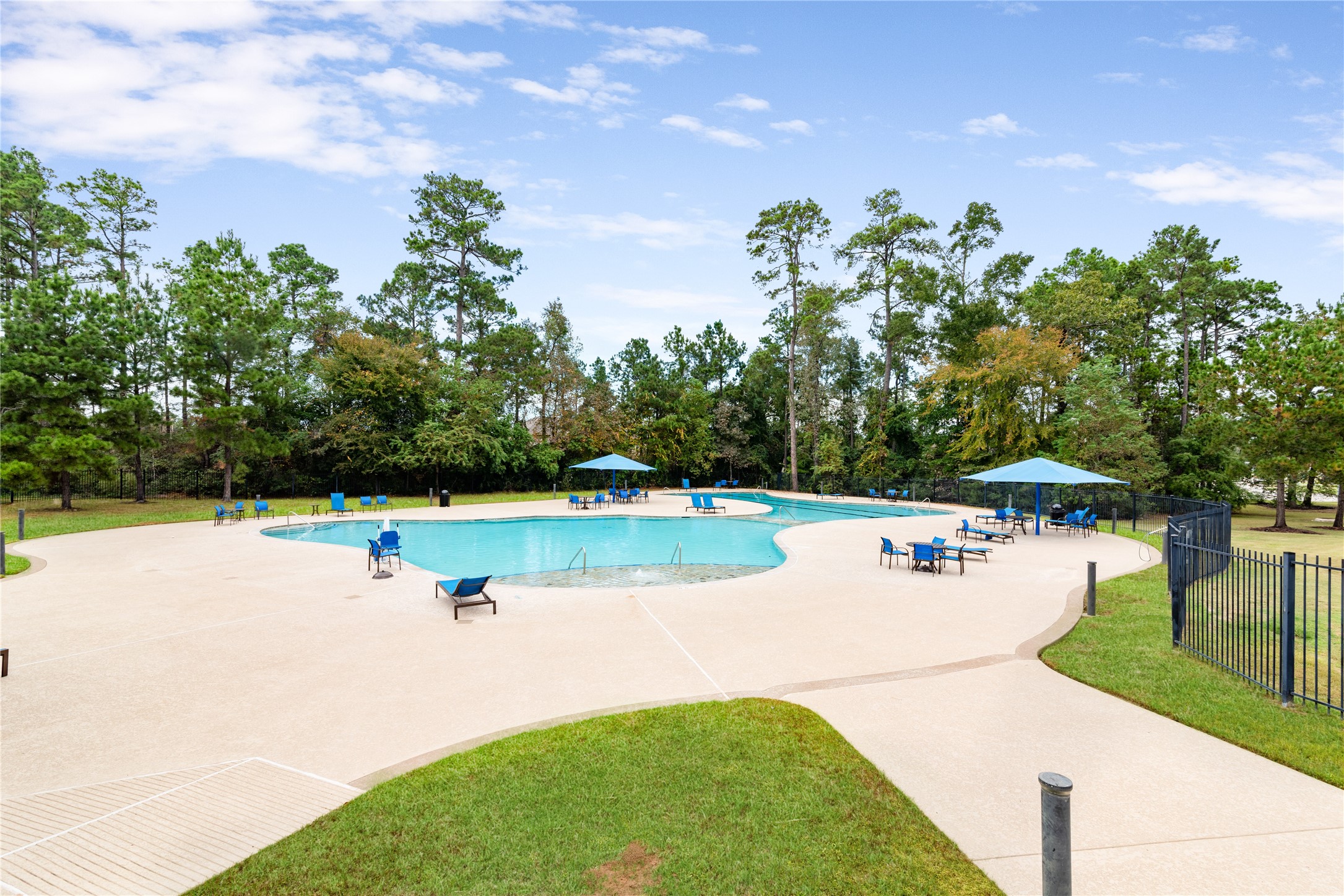 Expansive community pool surrounded by lush greenery, offering ample seating and shaded areas for relaxation.