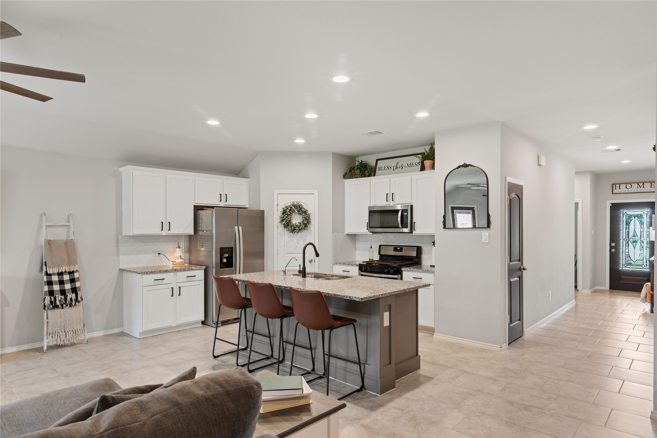 Spacious open-plan kitchen with modern white cabinetry, stainless steel appliances, and a central island with seating, seamlessly connecting to a welcoming entryway.