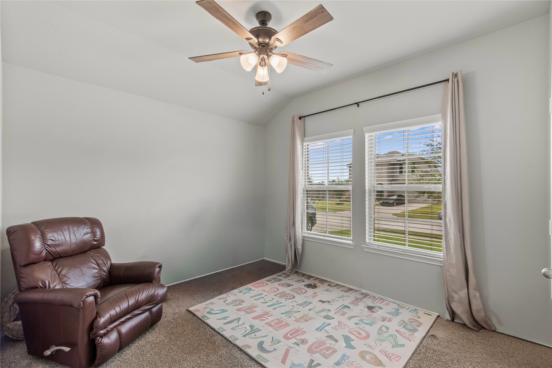 Cozy room with plush carpeting, a comfortable recliner, and large windows offering plenty of natural light. A ceiling fan adds comfort to this inviting space, ideal for relaxation or a home office.