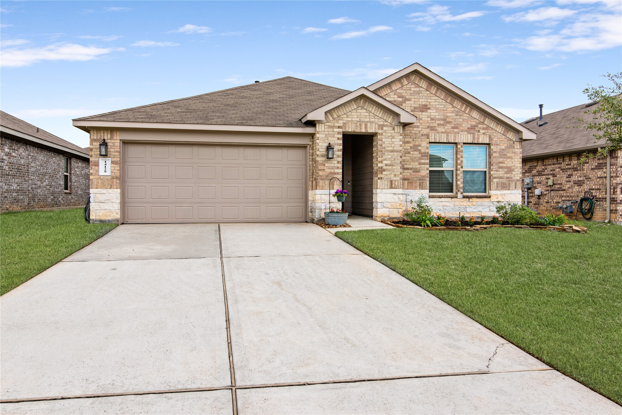 Charming single-story brick home with a two-car garage, featuring a well-maintained front yard and a welcoming entryway.