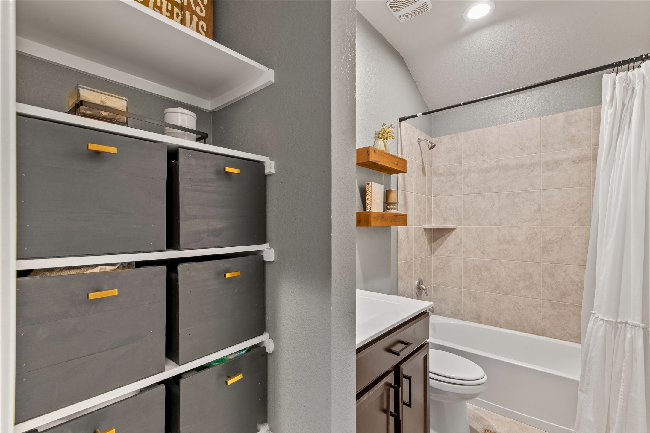 Modern bathroom with a sleek vanity, ample storage, and a tiled shower-tub combo.