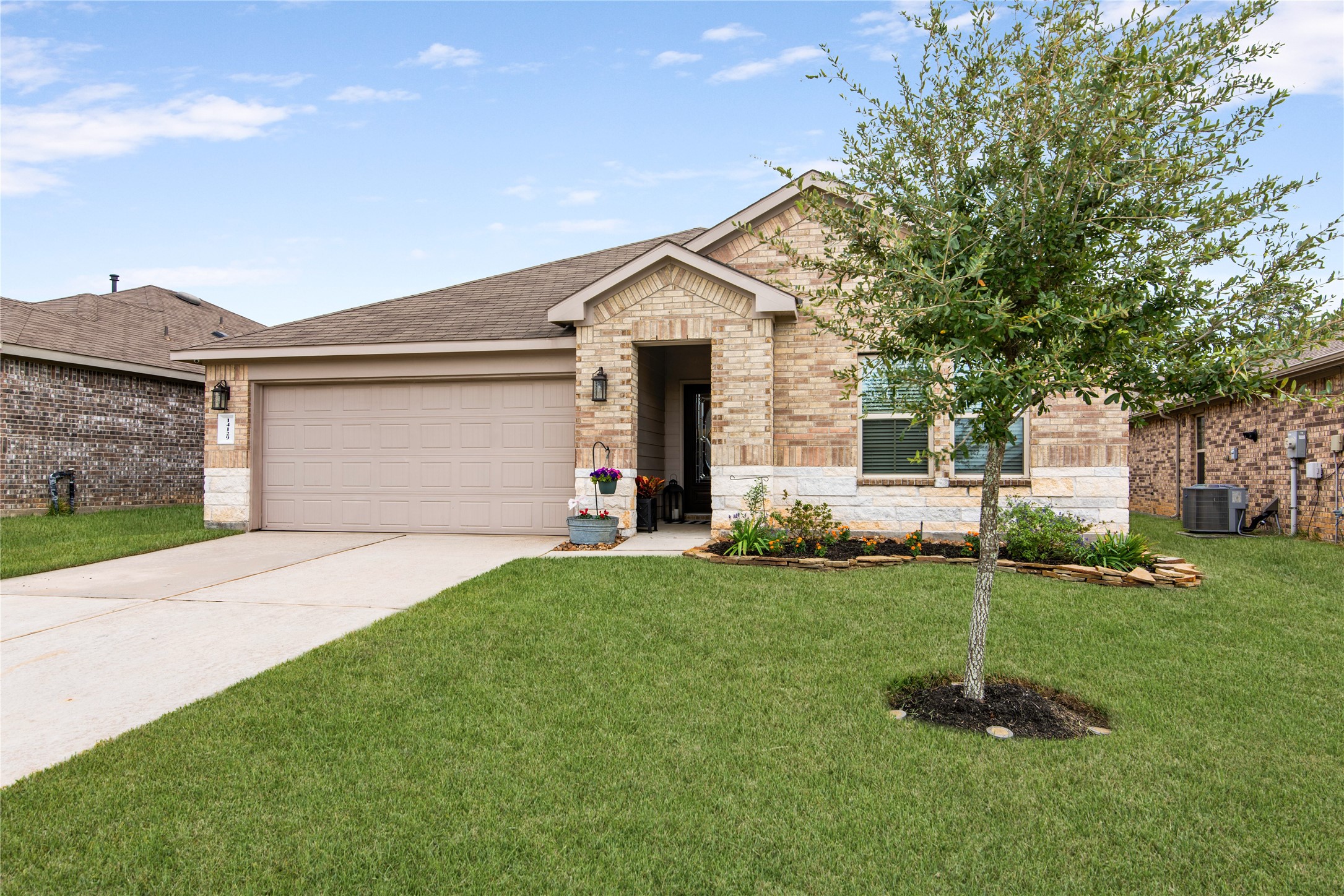 Charming brick home with a two-car garage, lush green lawn, and inviting landscaping, perfect for comfortable living.