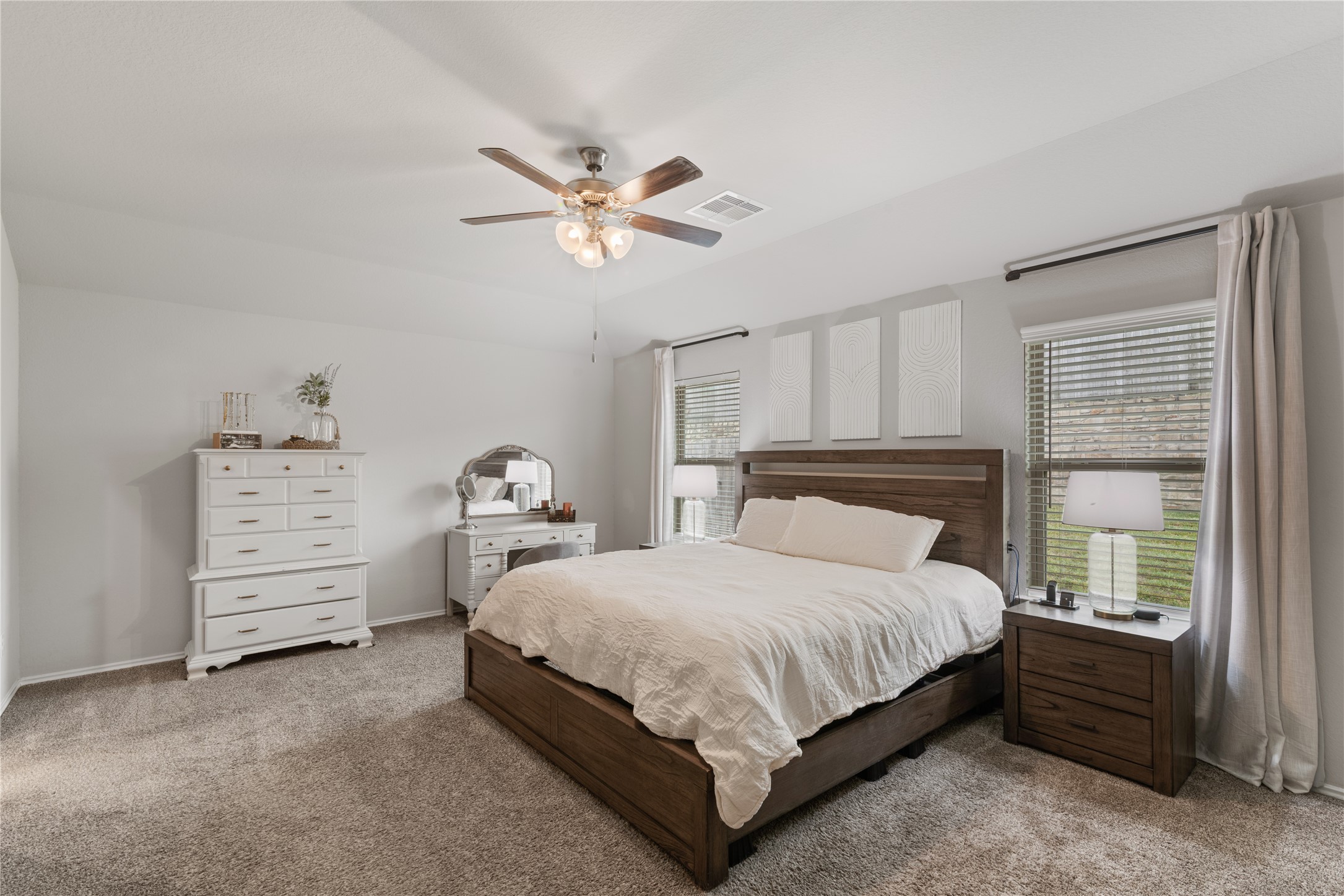 Spacious bedroom featuring a plush carpet, modern ceiling fan, and large windows that fill the room with natural light.