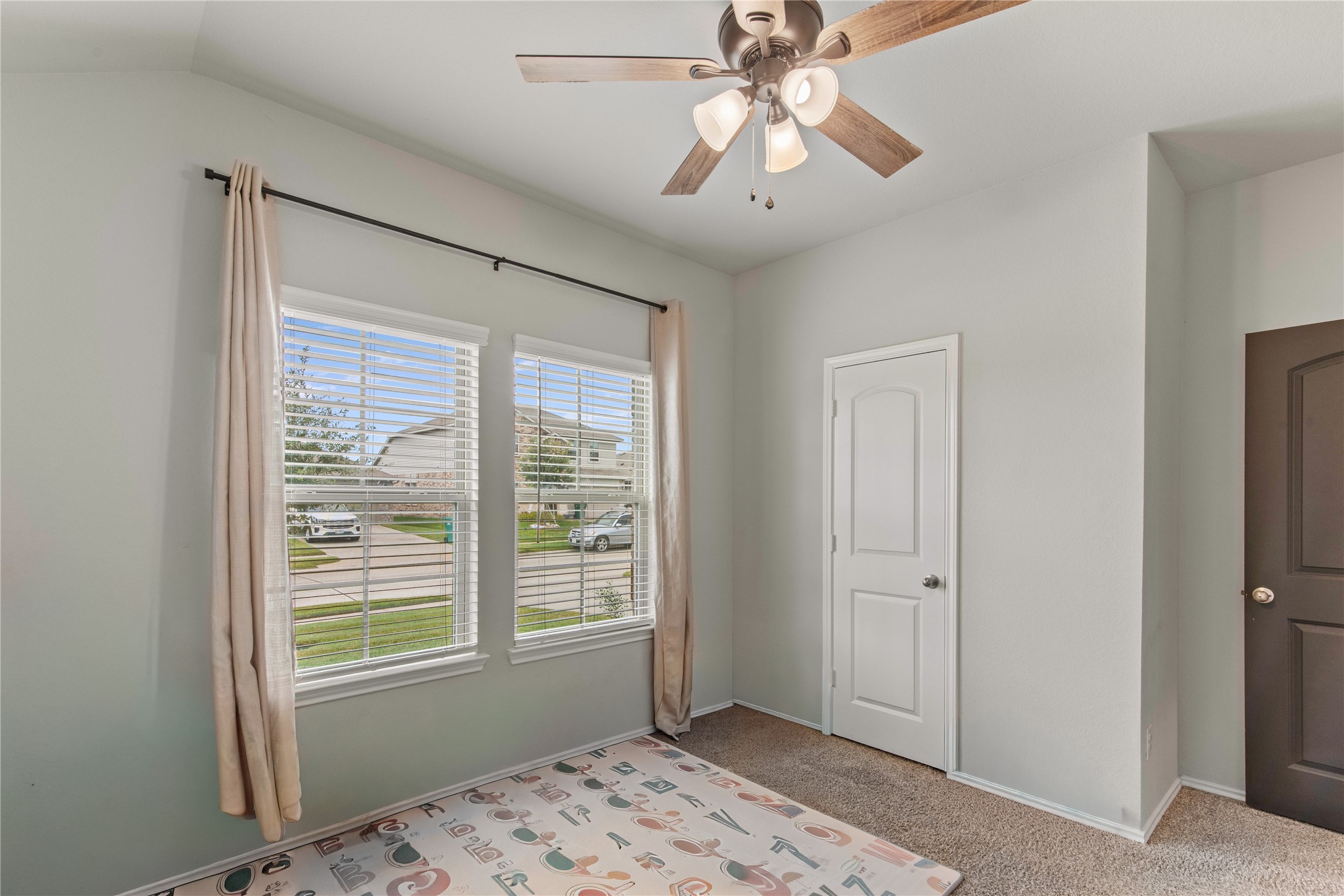 Bright and inviting room with large windows, neutral walls, and a ceiling fan, perfect for versatile use.