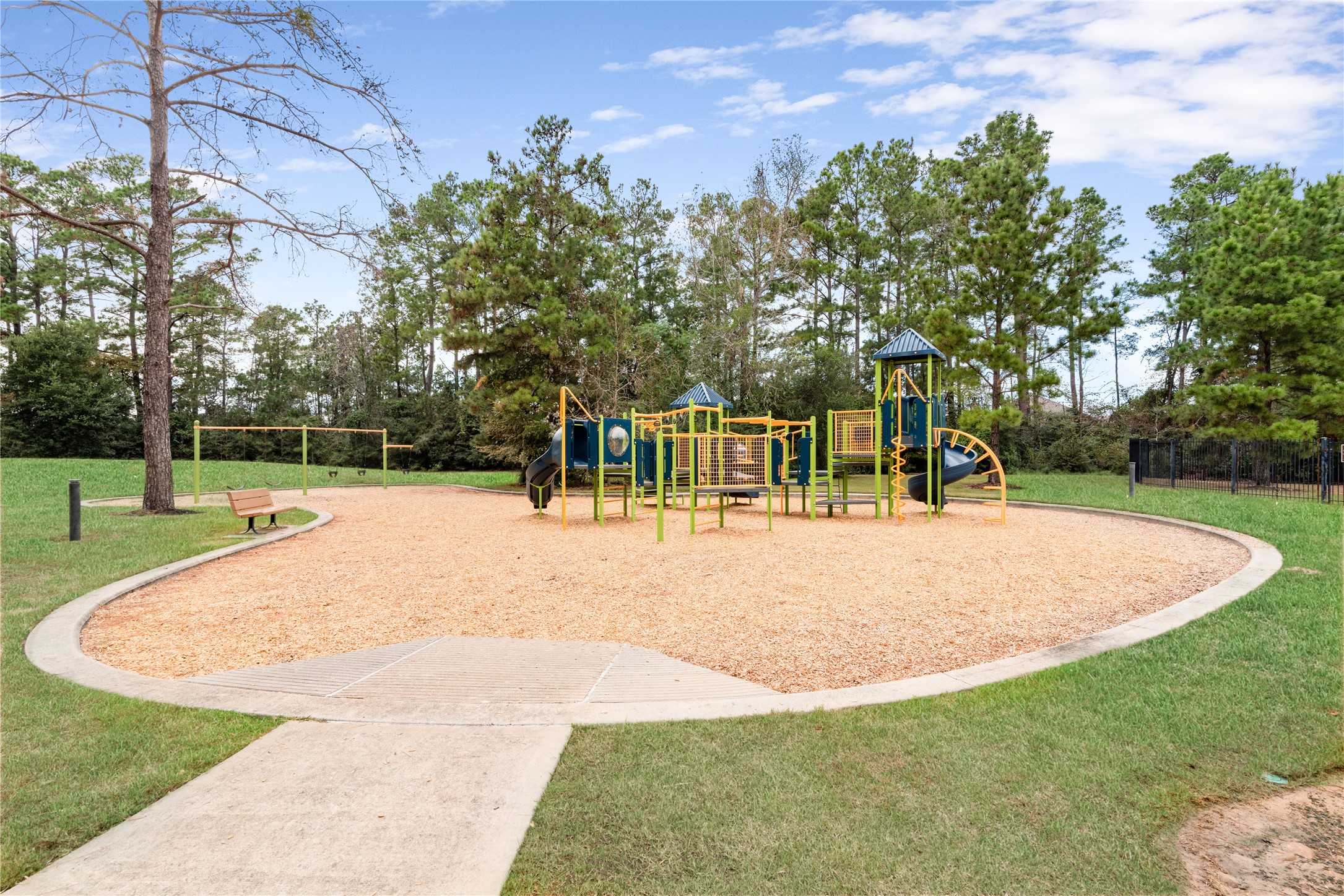 Charming playground nestled among lush trees, featuring vibrant equipment and a serene bench area, perfect for family fun.